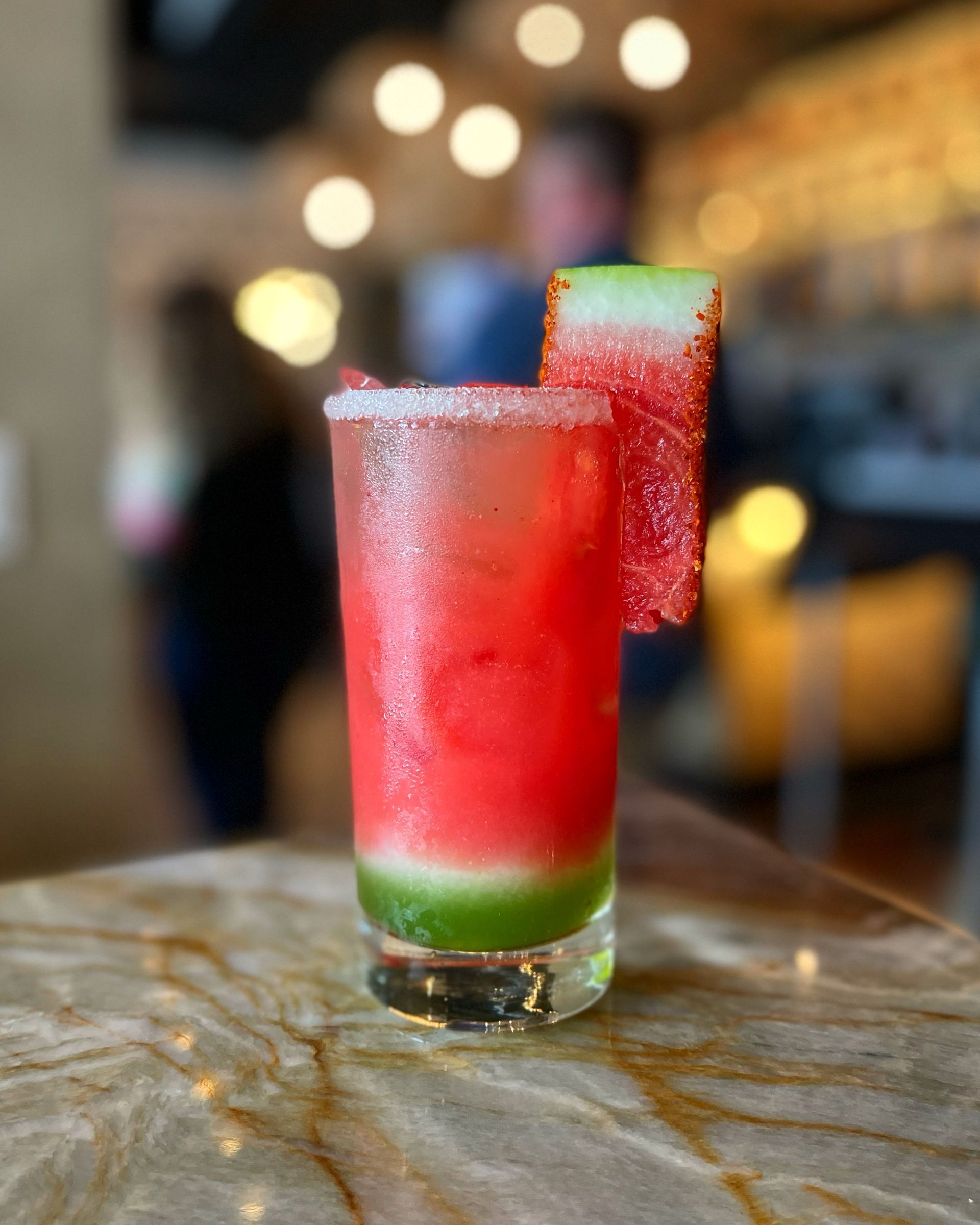 A watermelon drink in a tall glass with a slice of watermelon on the rim.