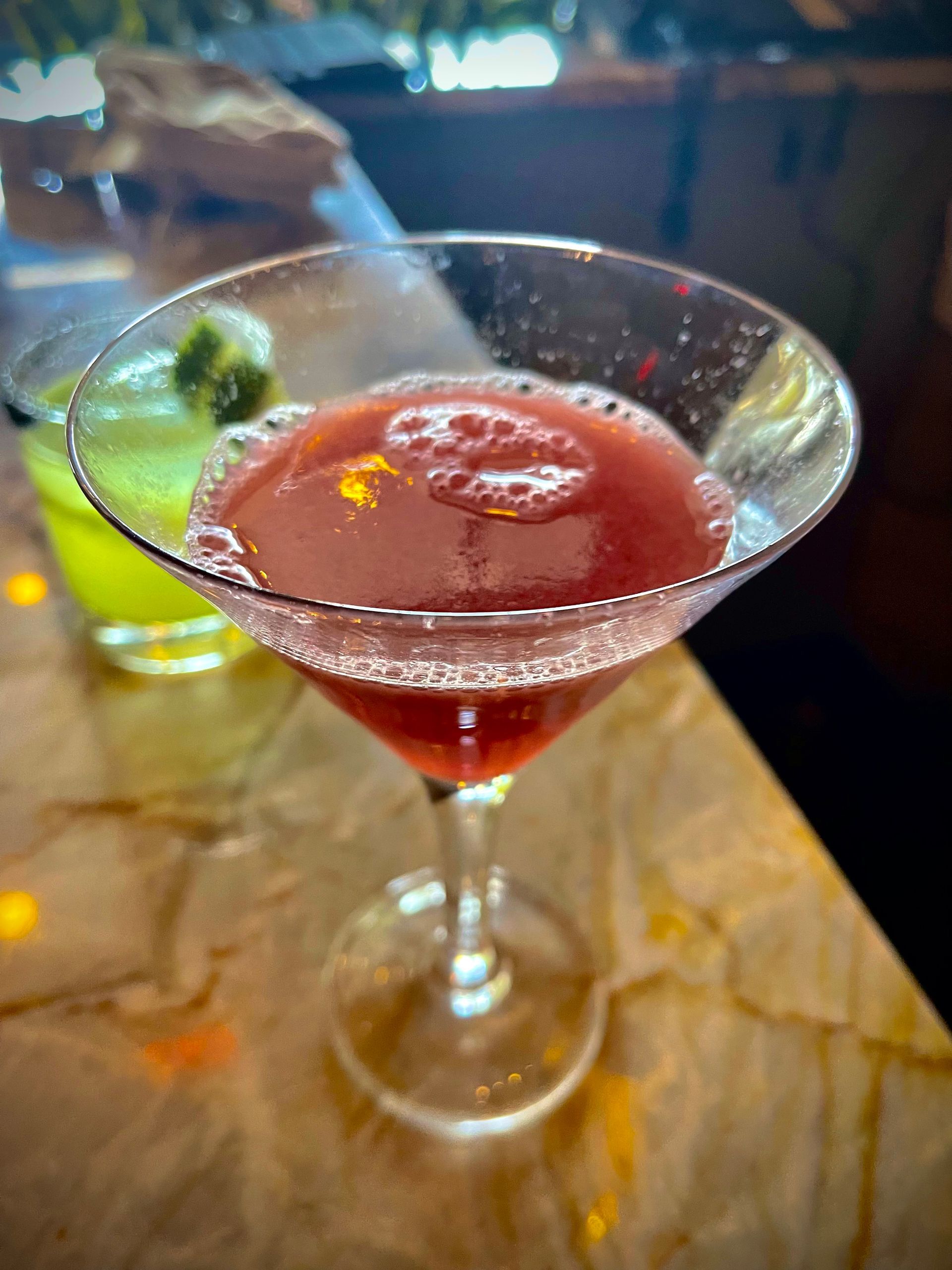 A martini glass filled with a red liquid is on a table.