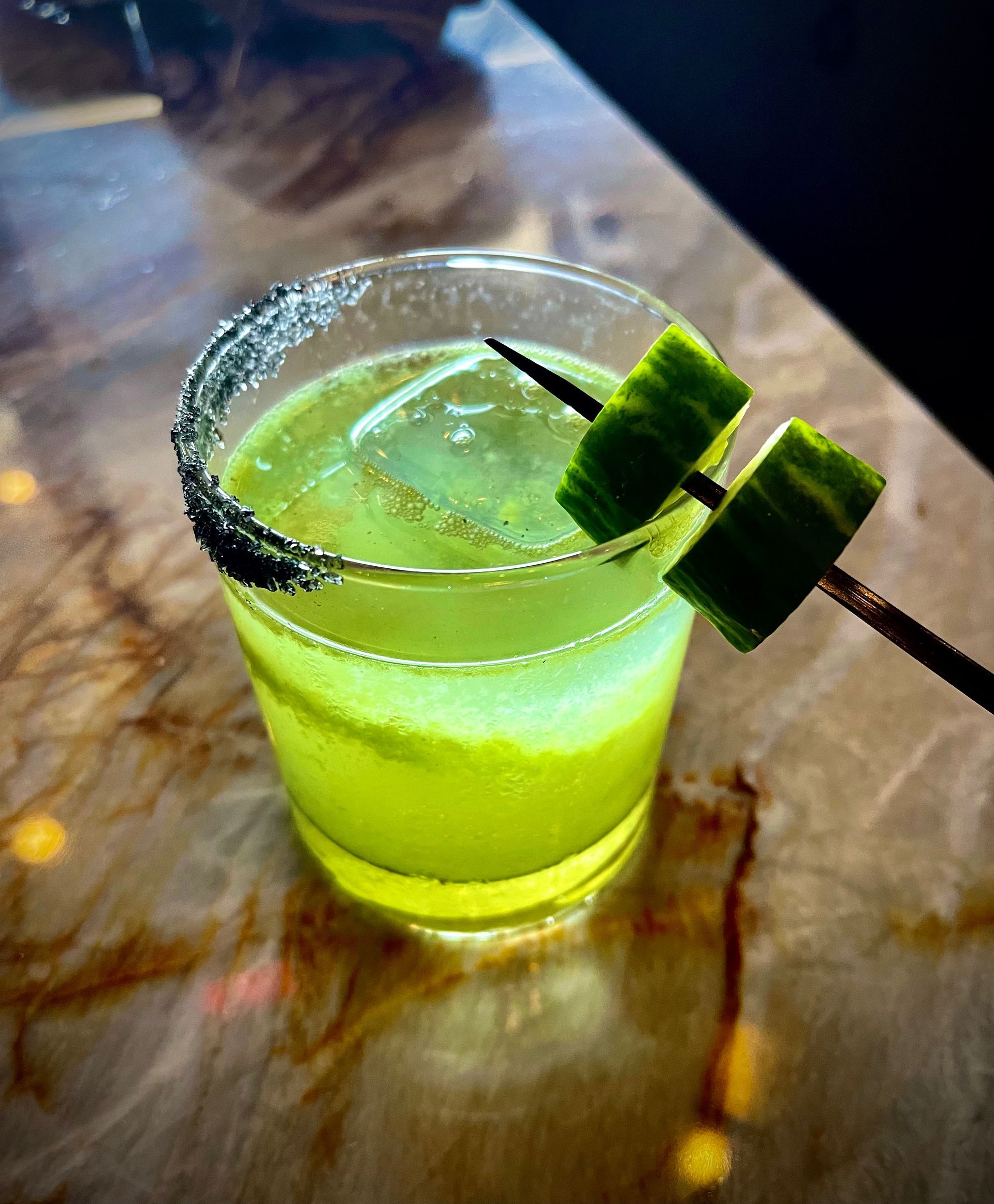 A green drink with a cucumber on a toothpick on a table