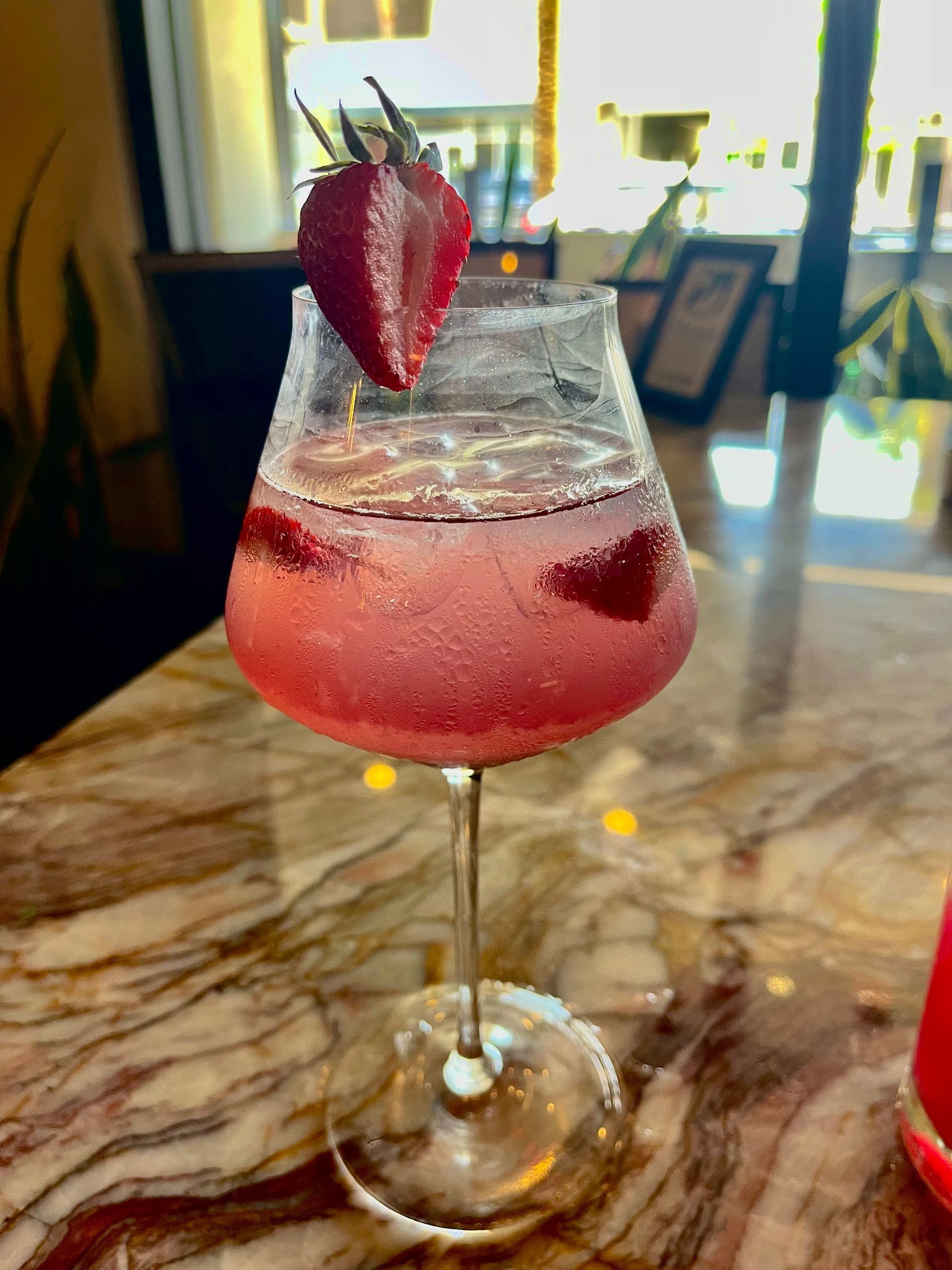 A glass of pink liquid with a strawberry on top on a table.