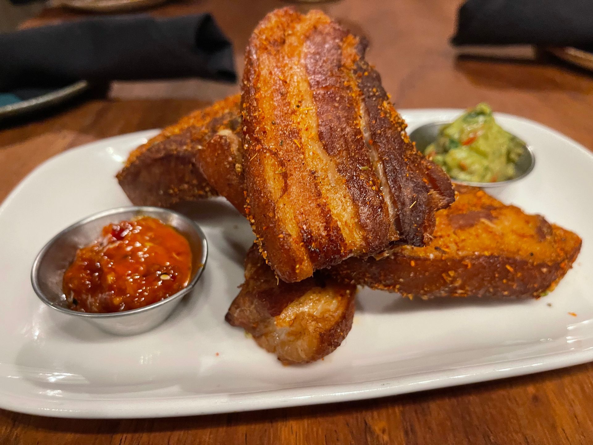 A white plate topped with fried bacon and guacamole on a wooden table.