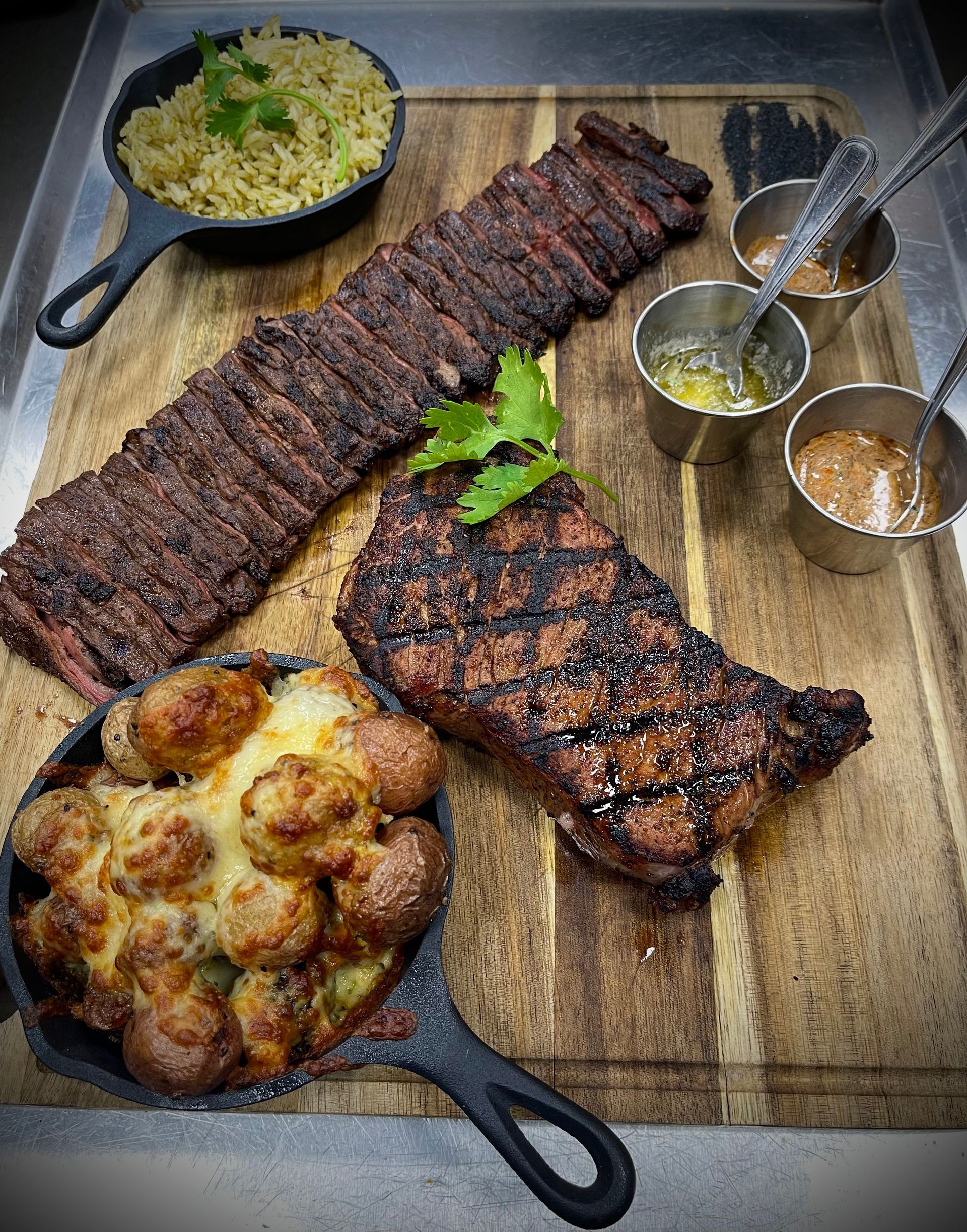 A wooden cutting board topped with steaks , potatoes , and rice.