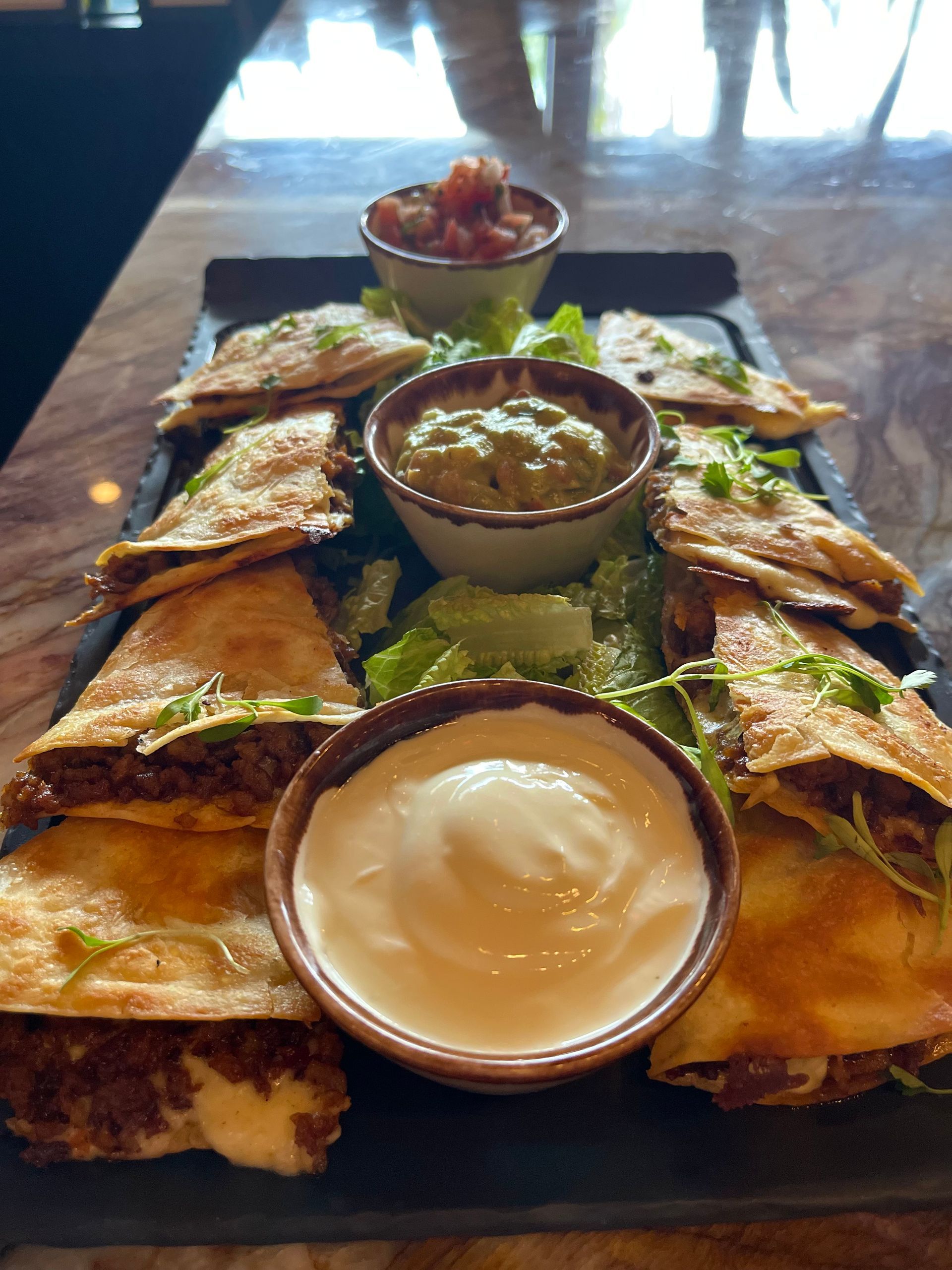 A tray of quesadillas with guacamole and sour cream on a table.