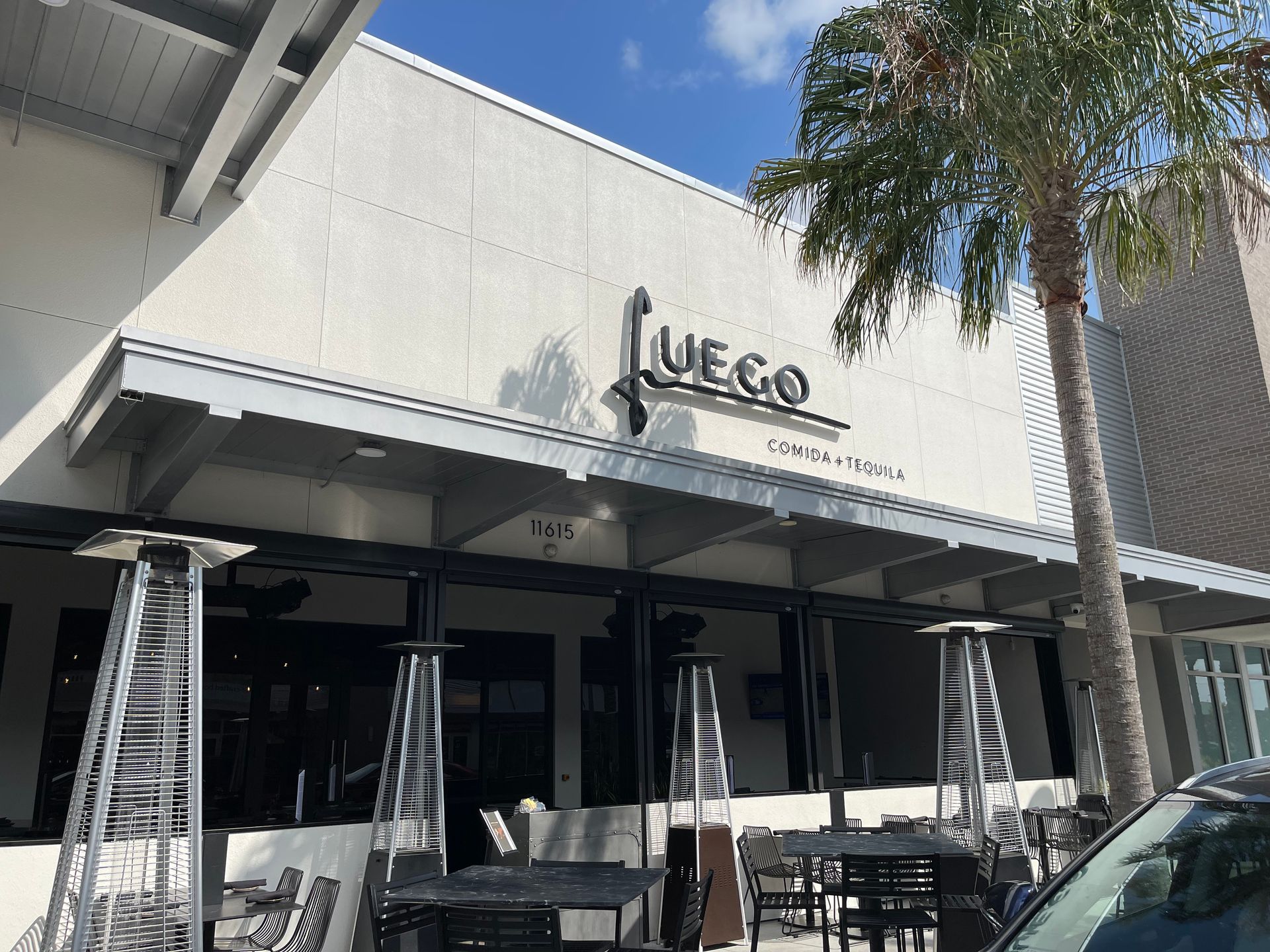A restaurant with tables and chairs outside and a car parked in front of it.