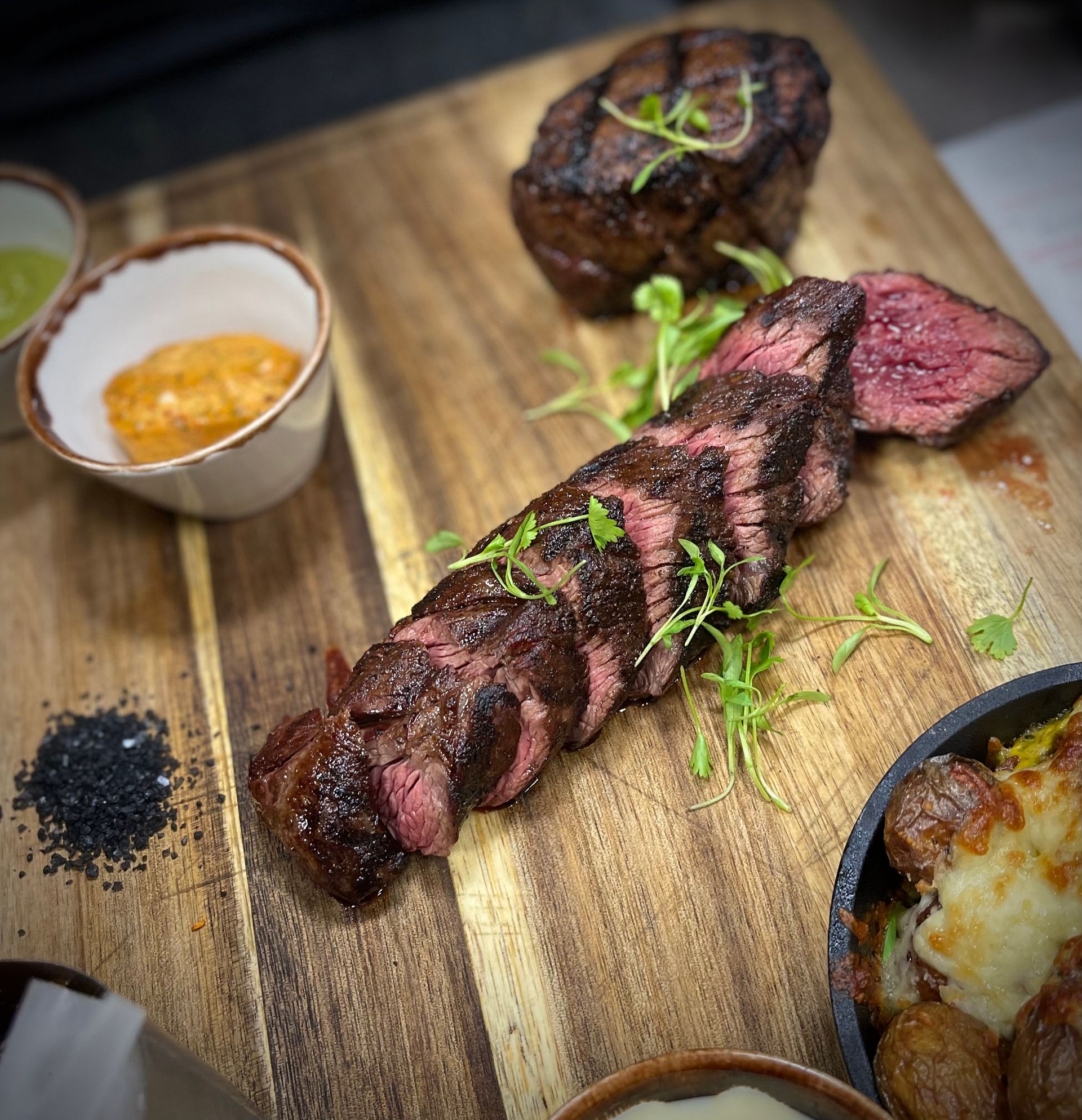 A steak is sitting on a wooden cutting board next to a bowl of sauce.