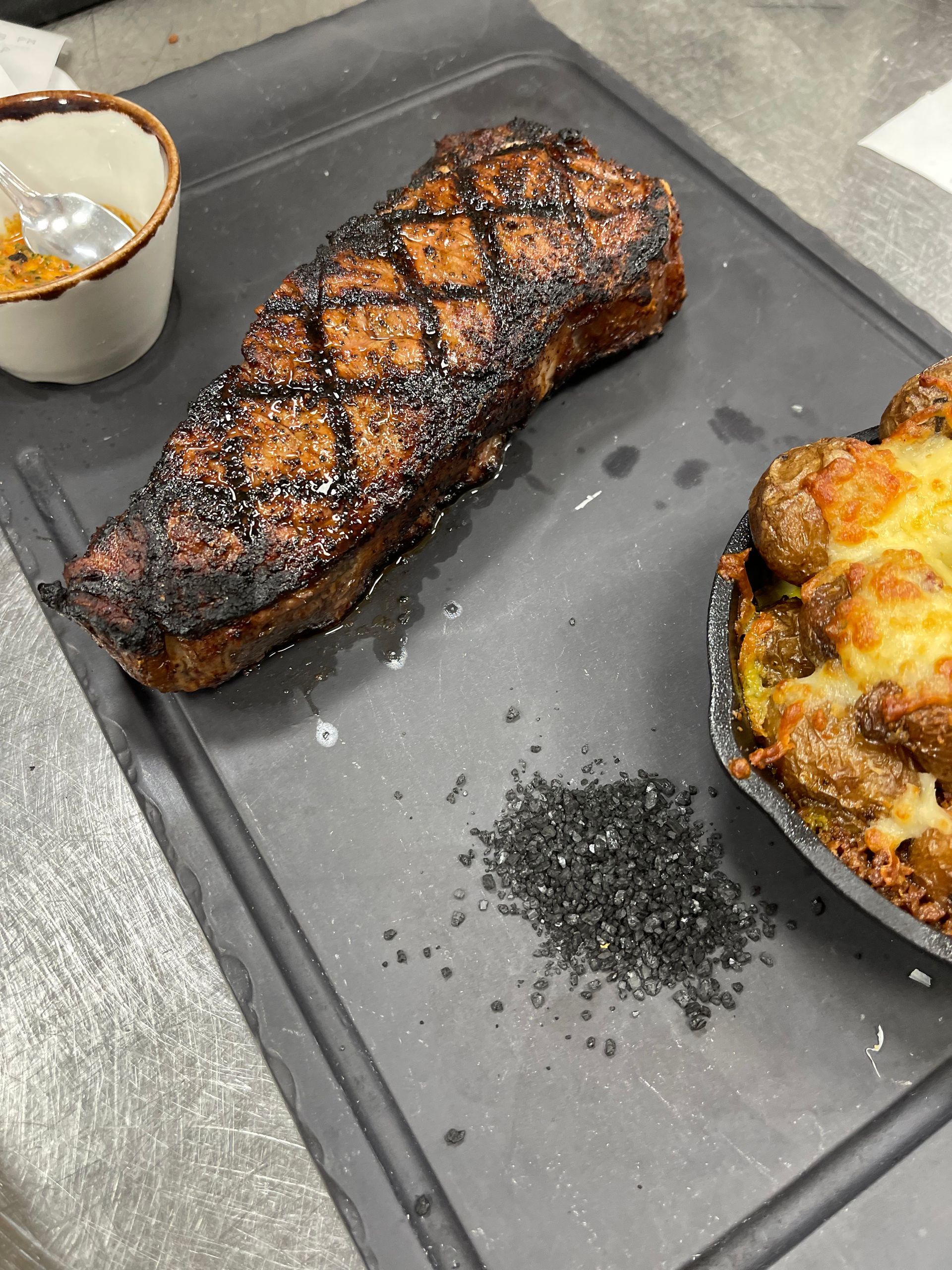 A steak is sitting on a cutting board next to a bowl of sauce.