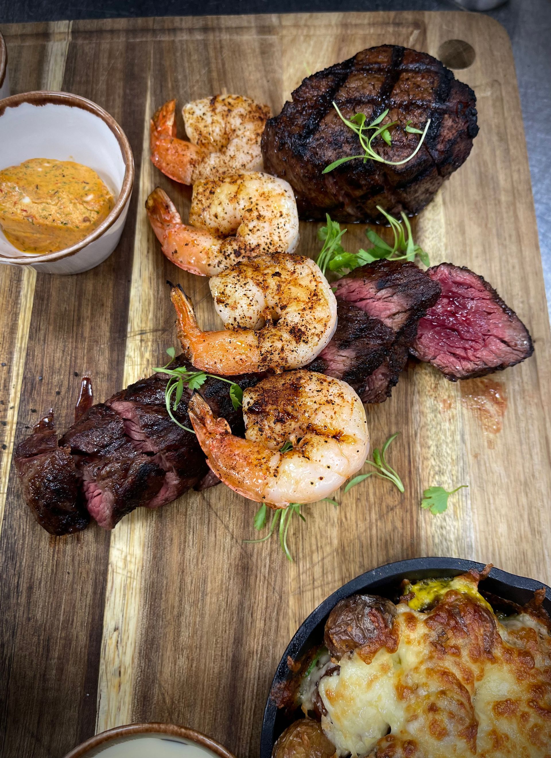 A wooden cutting board topped with meat and shrimp.