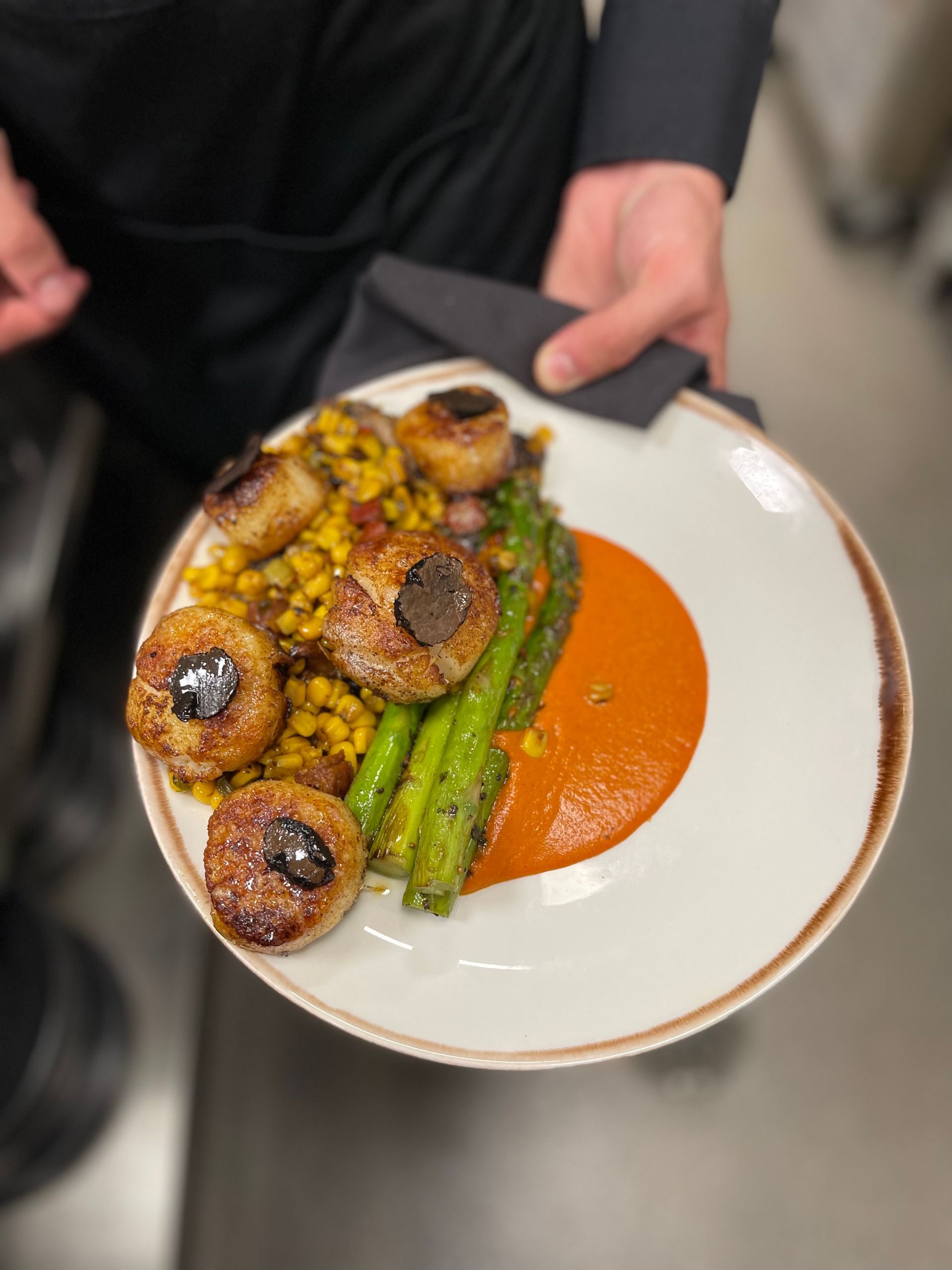 A person is holding a plate of food with meatballs and asparagus.