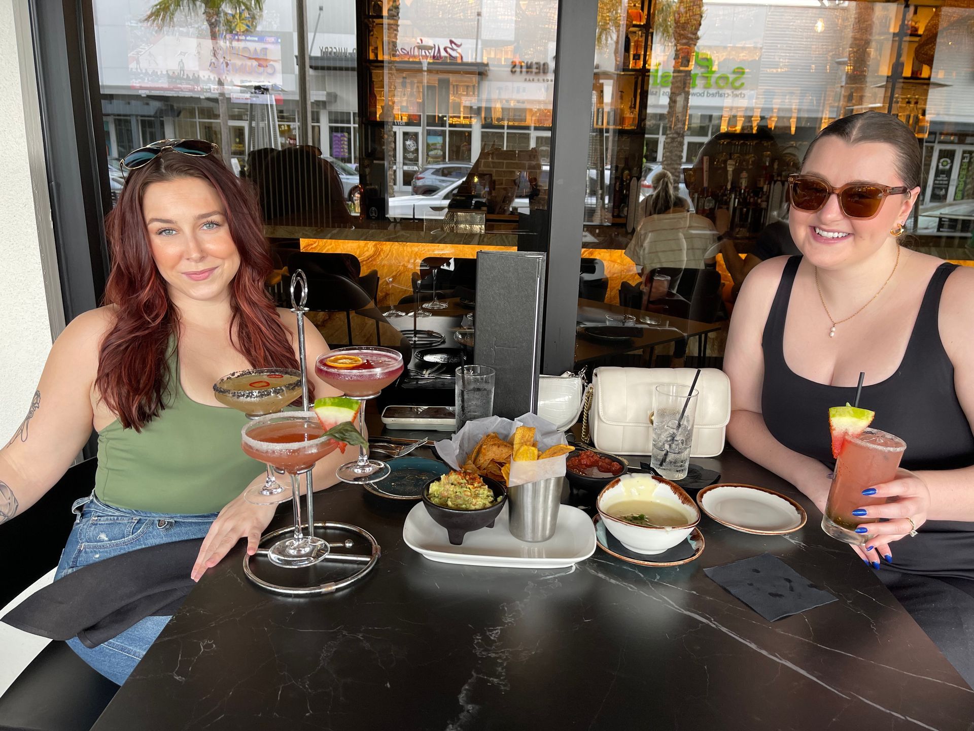 Two women are sitting at a table with drinks and food.