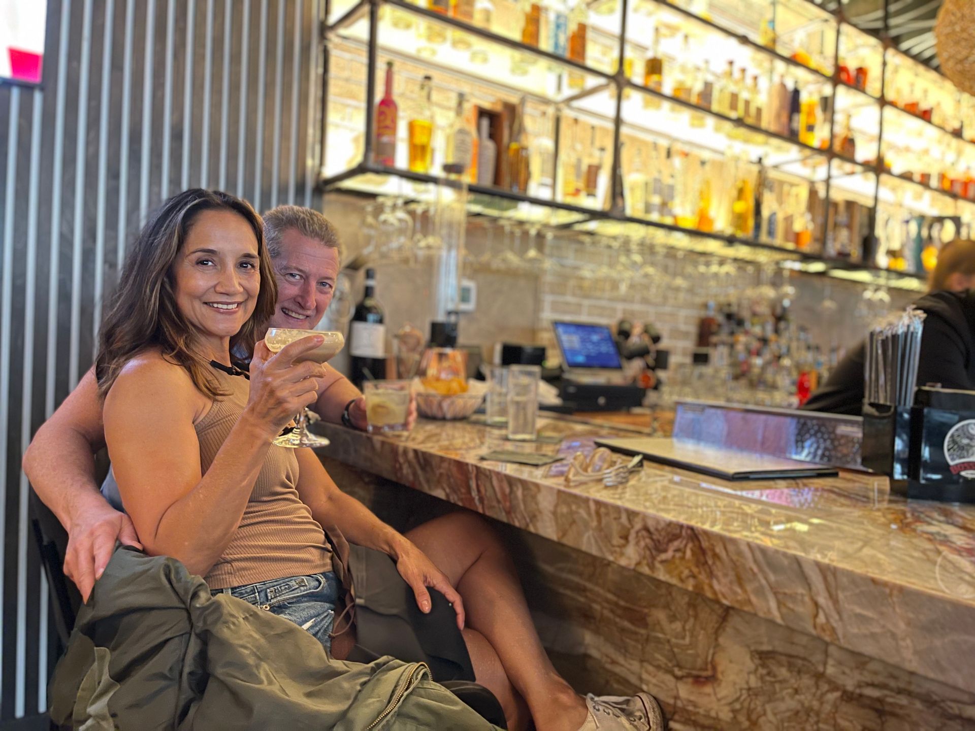 A man and a woman are sitting at a bar holding drinks.