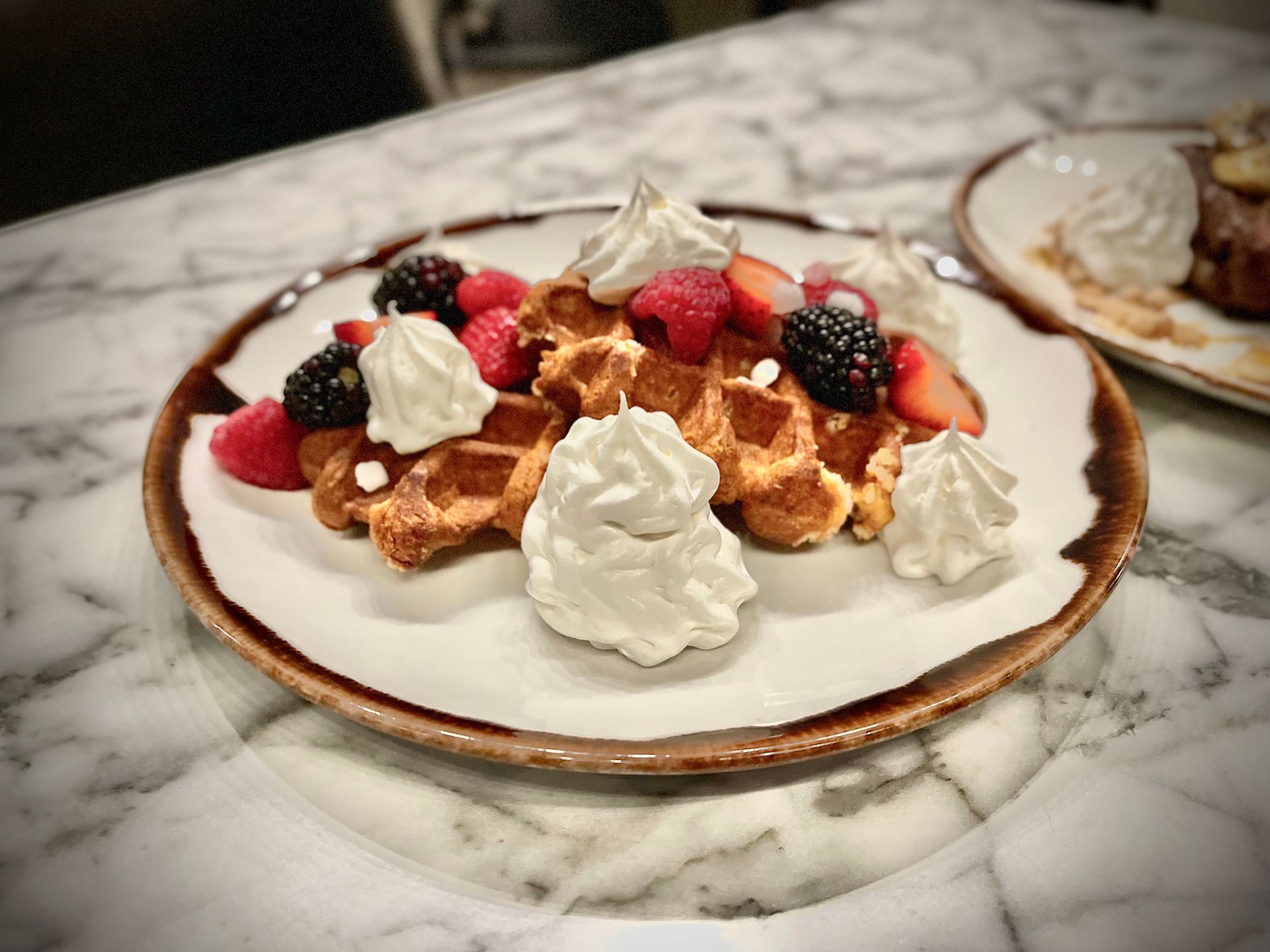 A plate of waffles with whipped cream and berries on a table.
