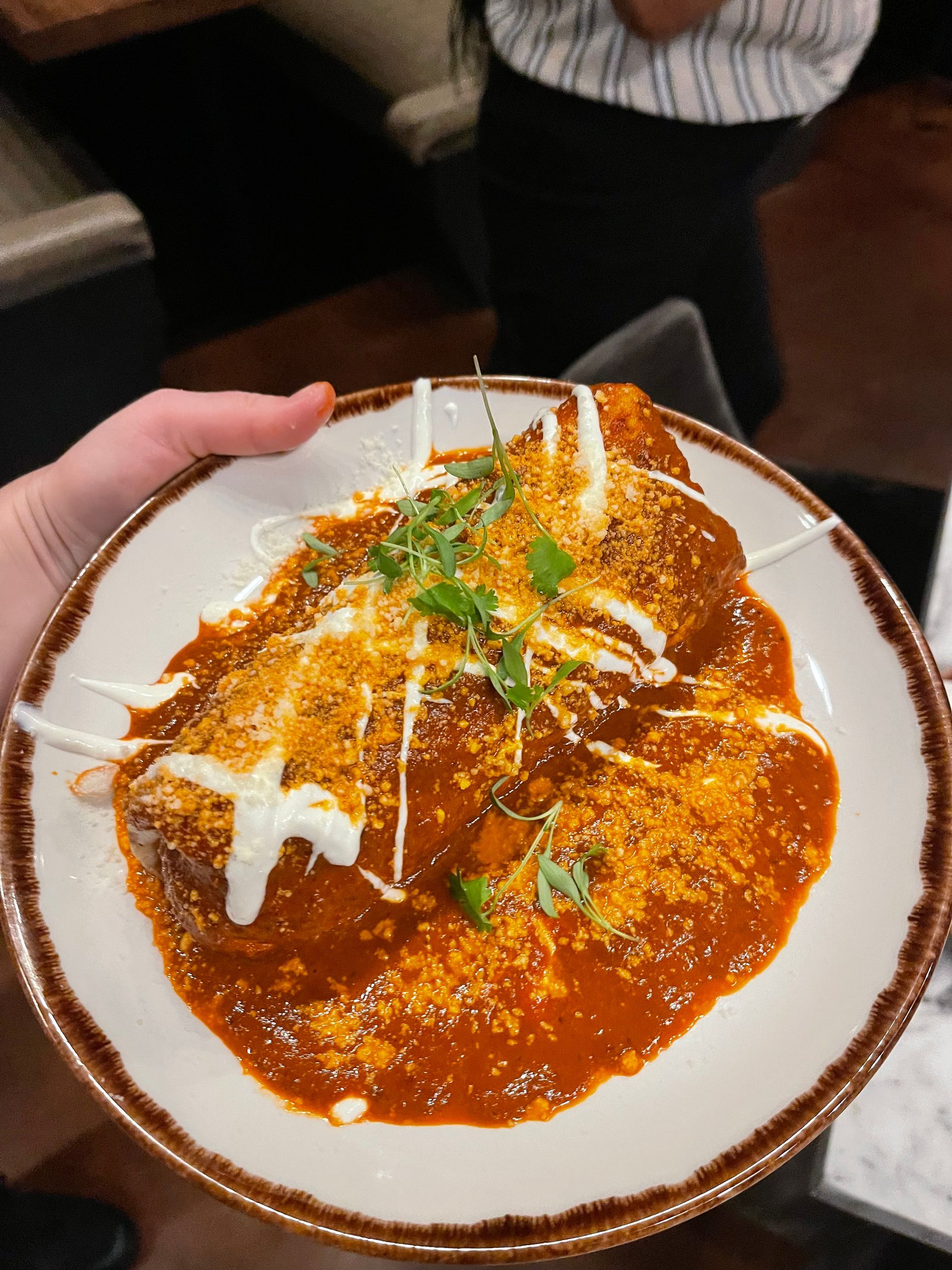 A person is holding a plate of food with sauce and cheese on it.