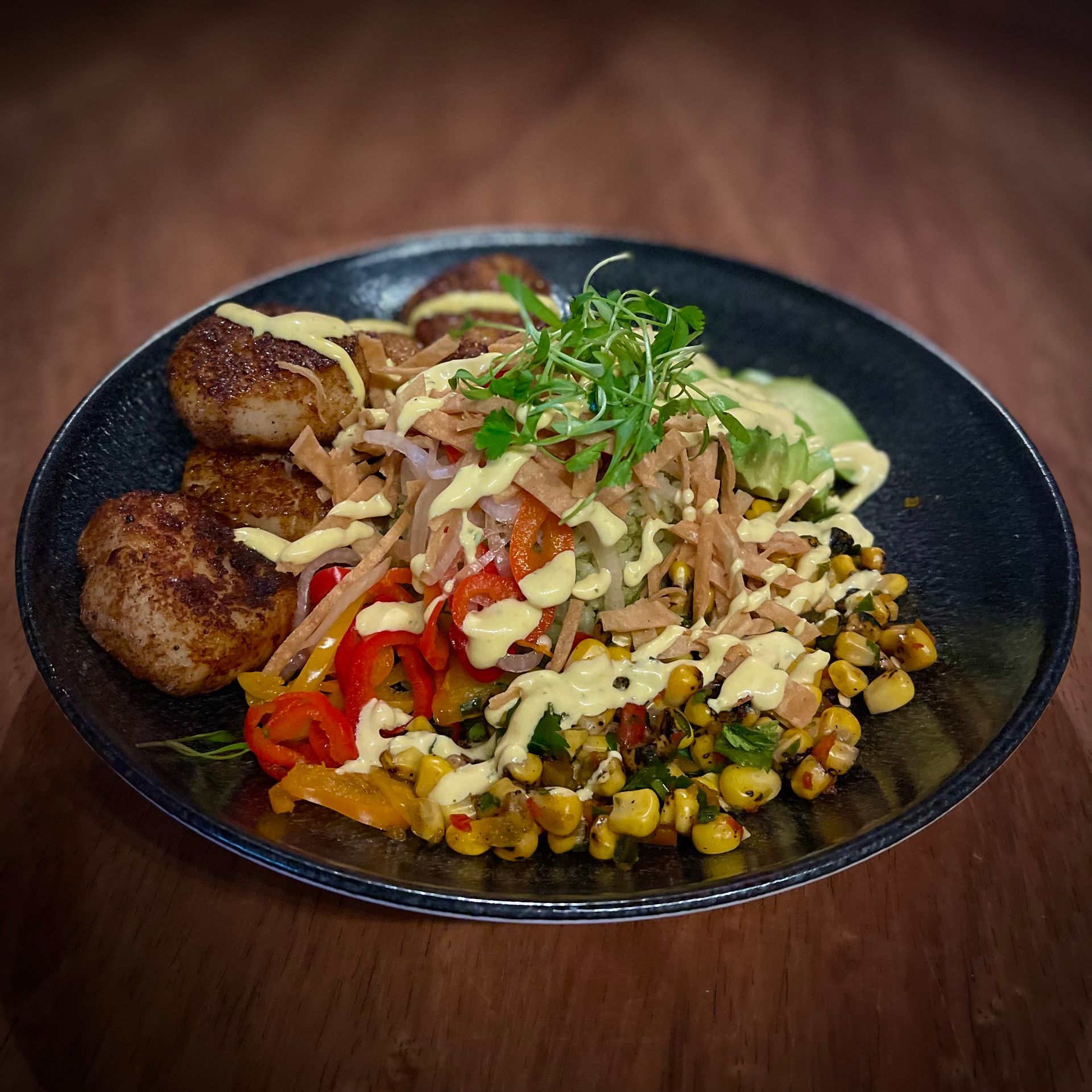 A black plate topped with meatballs , corn , and vegetables on a wooden table.