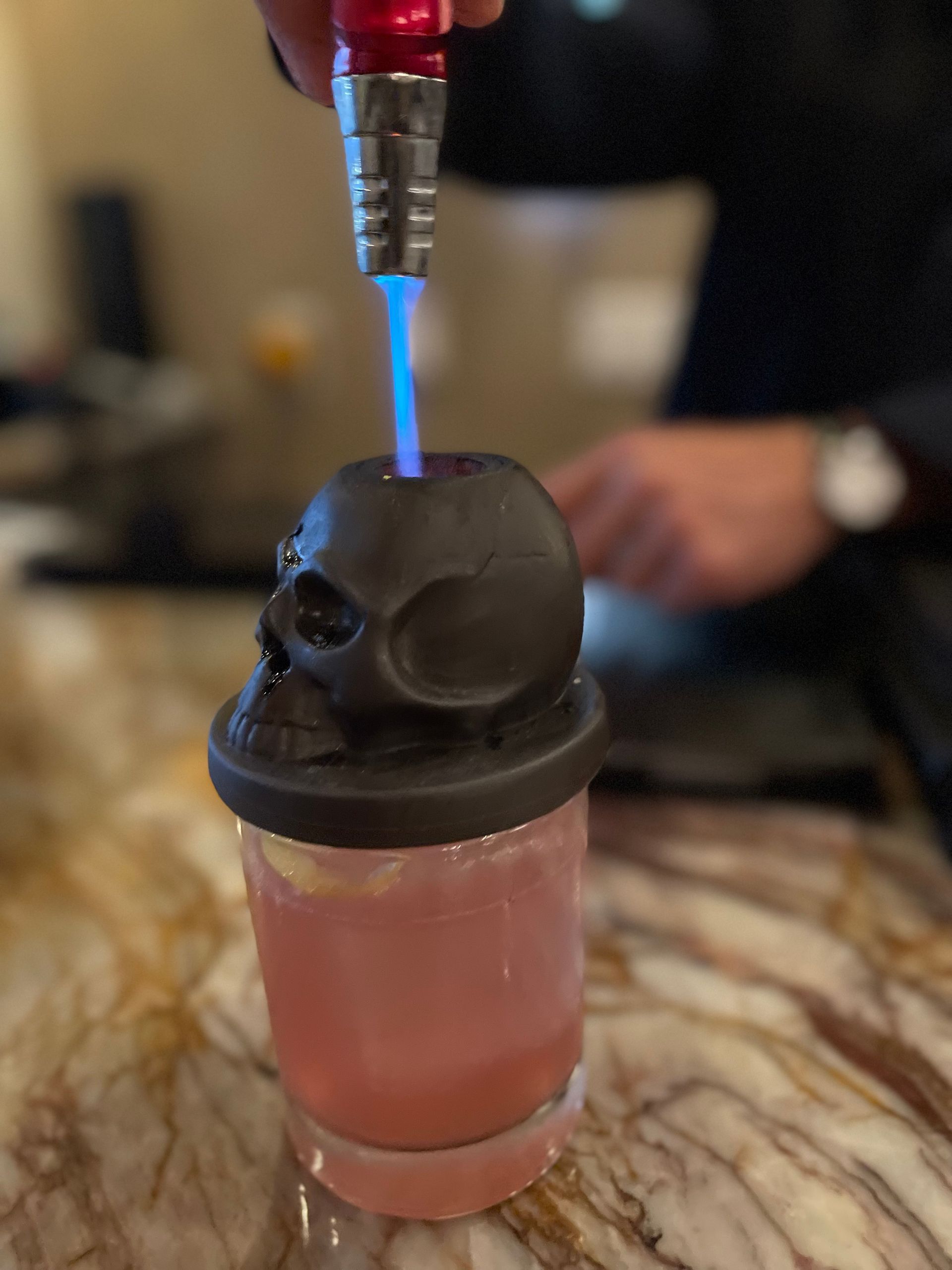 A person is pouring a drink into a glass with a skull on top.