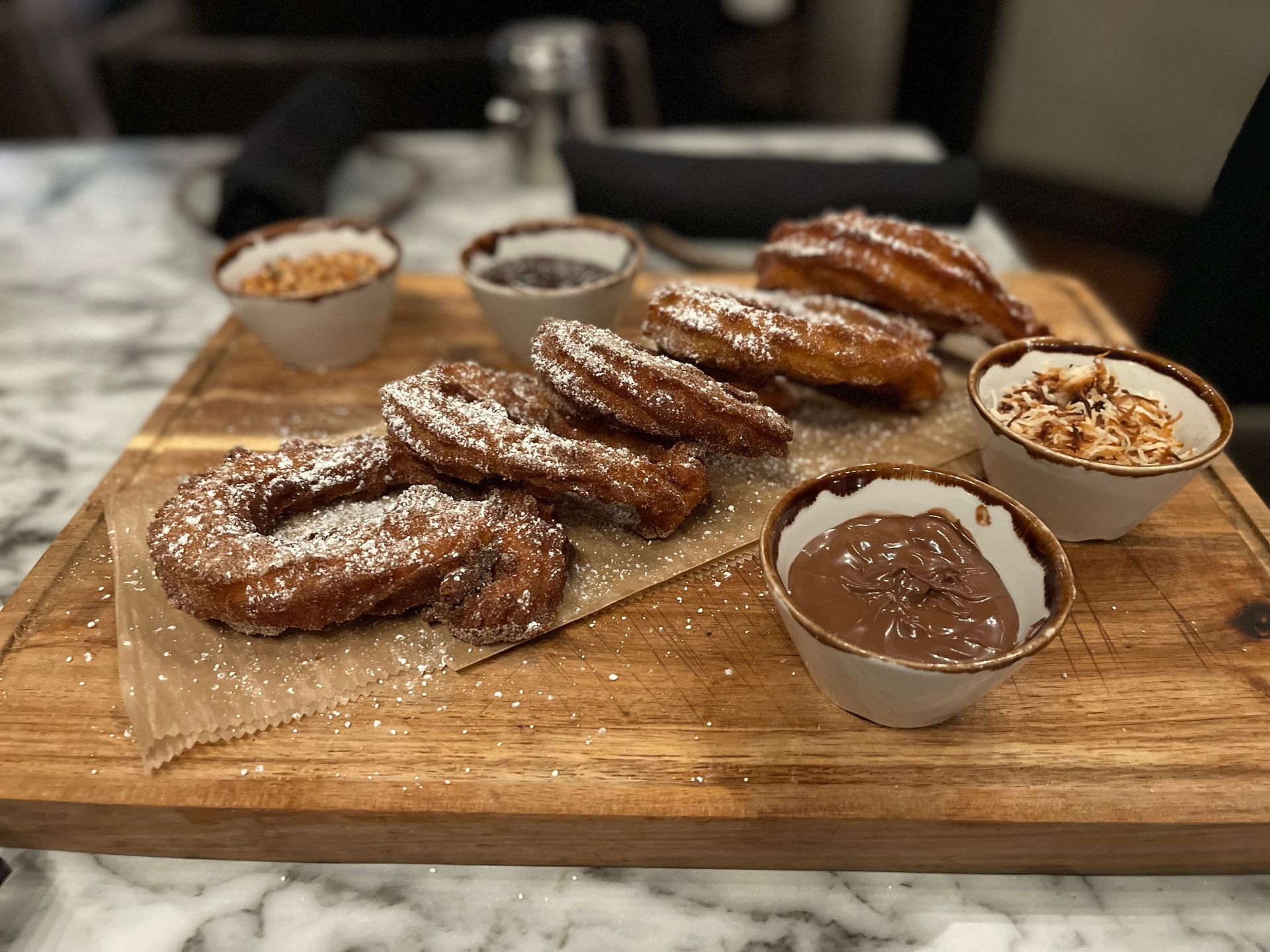 Churros with powdered sugar, served with dipping sauces on a wooden board.
