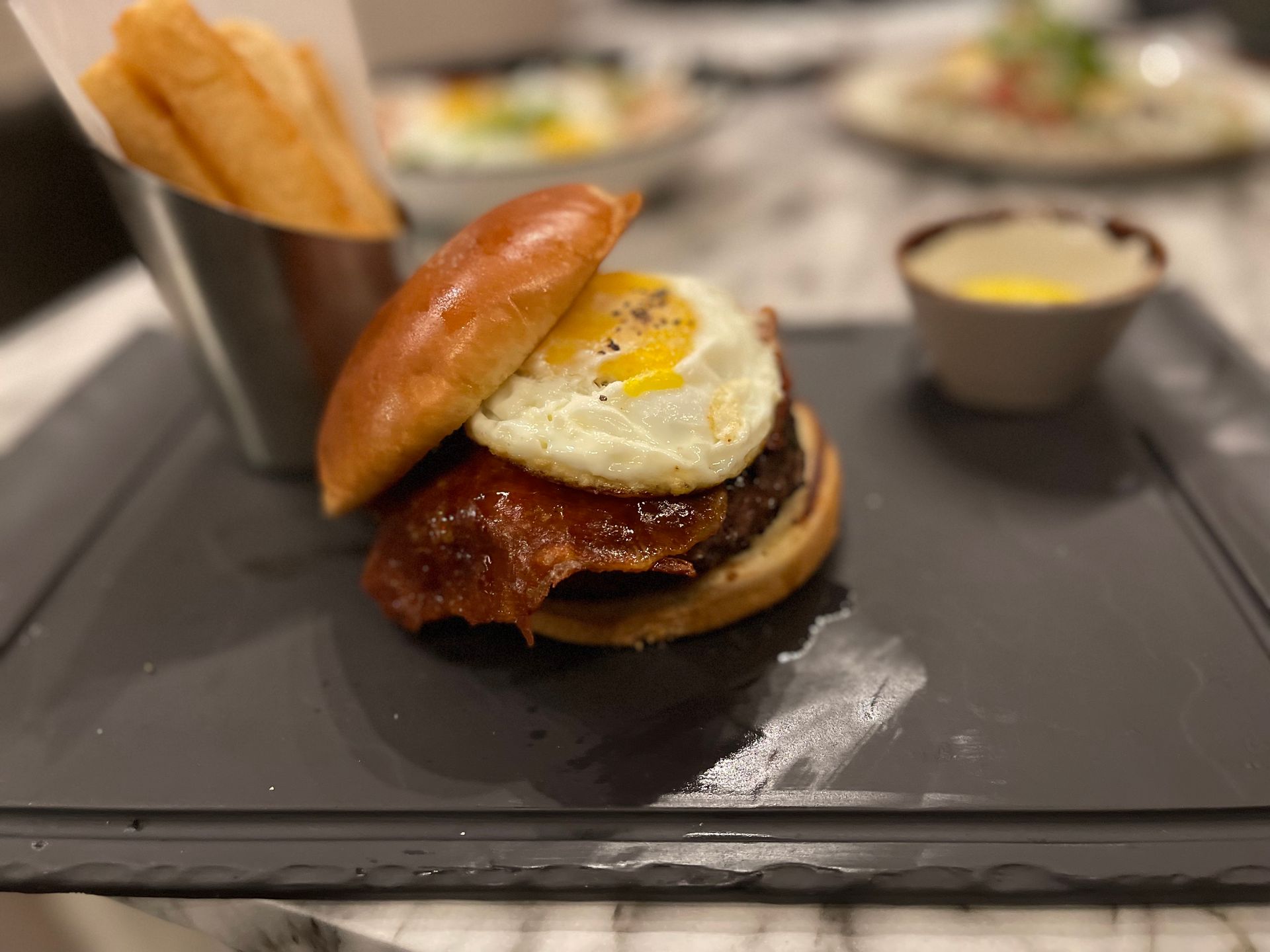 A close up of a hamburger with eggs and bacon on a plate