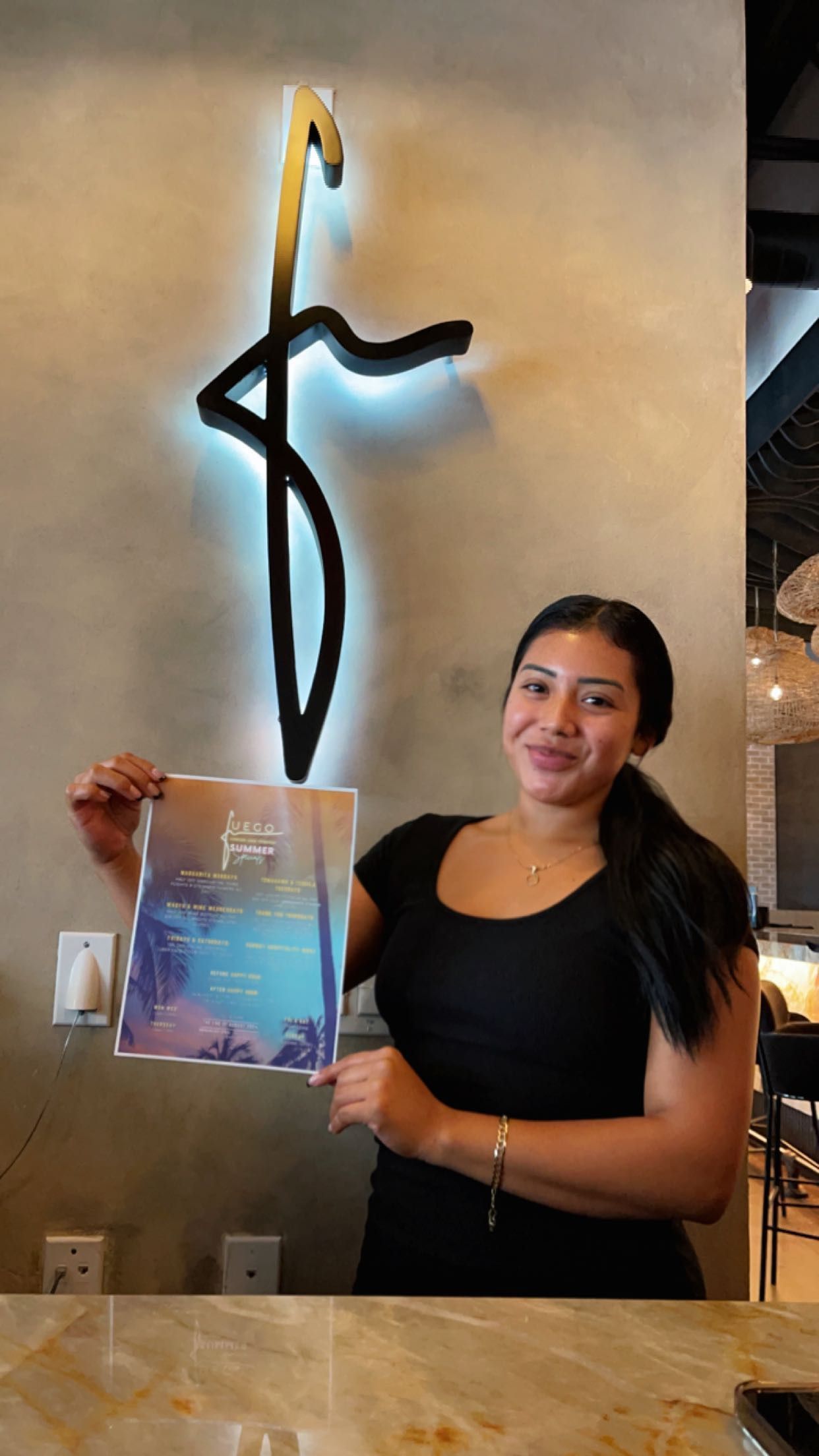 A woman is holding a book in front of a wall with a cross on it.