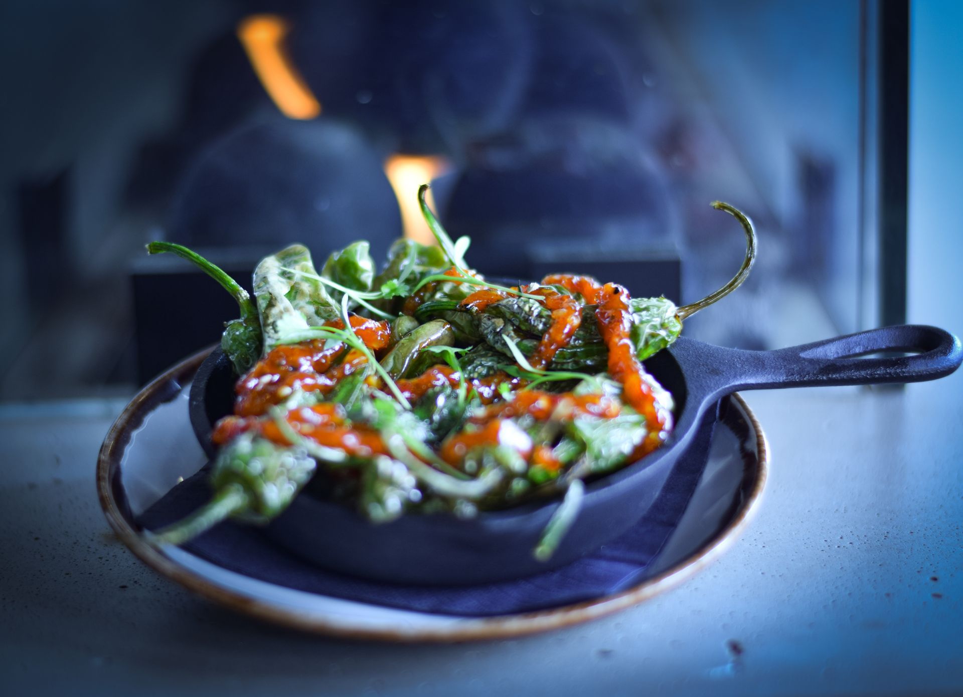 A skillet filled with vegetables and sauce is on a plate in front of a fireplace.