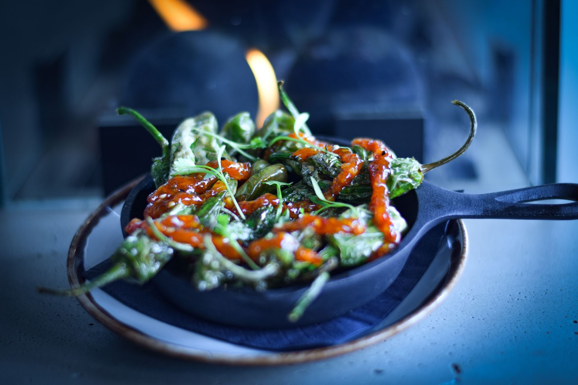 A skillet filled with vegetables is sitting on a plate in front of a fireplace.