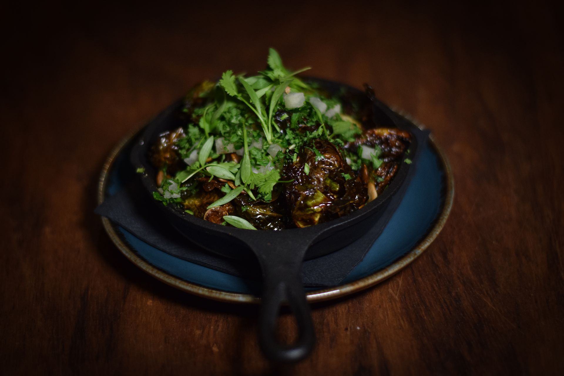 A skillet filled with food is on a plate on a wooden table.