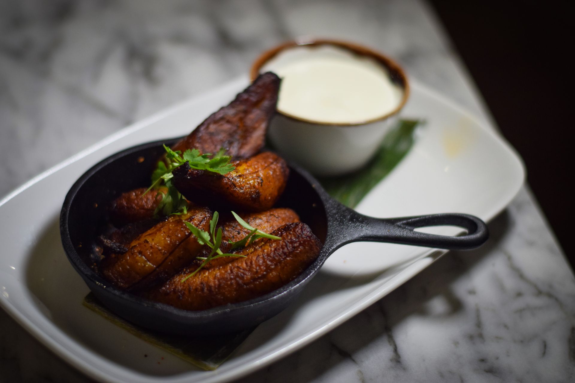 A pan filled with fried plantains next to a bowl of ranch dressing.