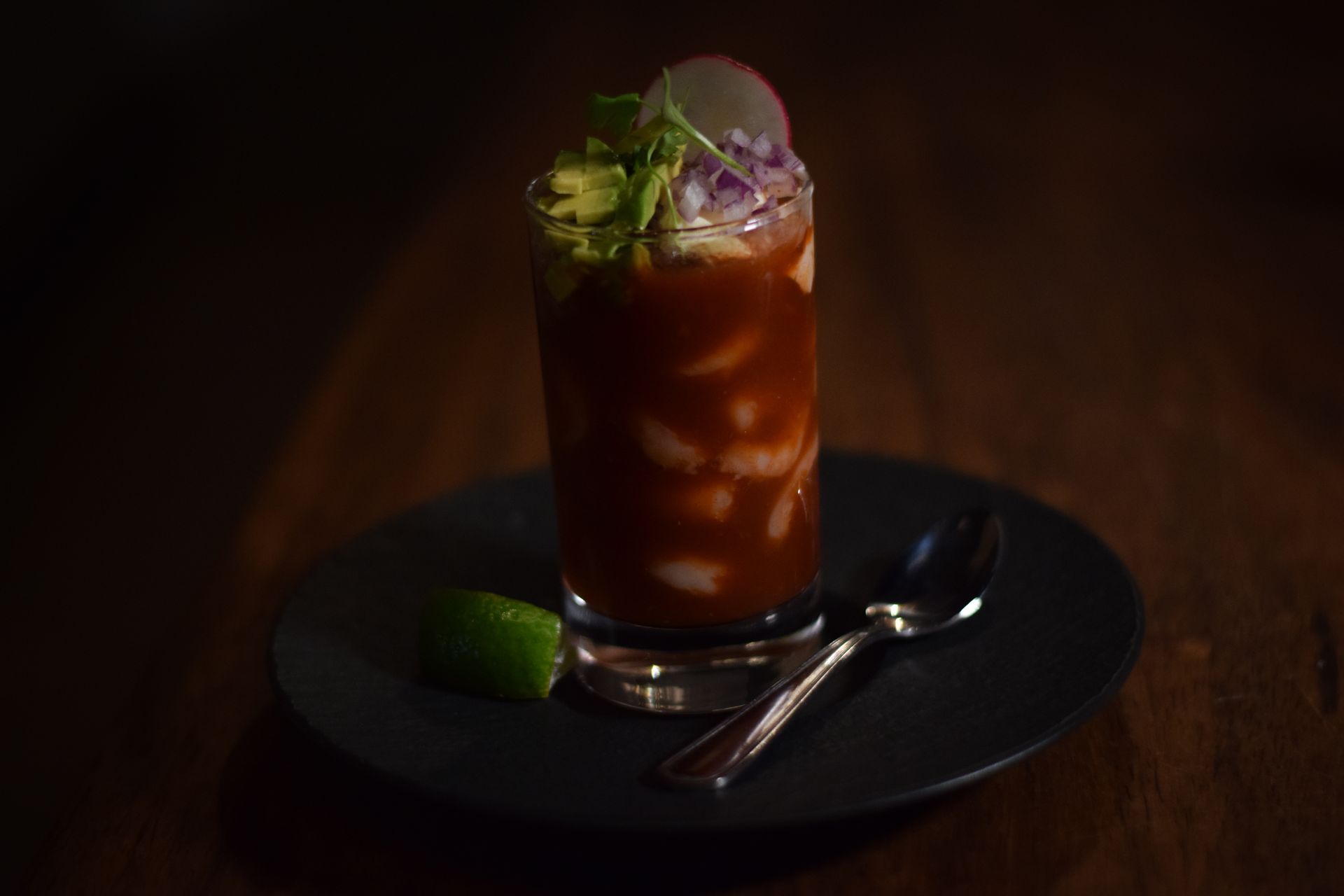 A close up of a drink in a glass on a plate with a spoon.