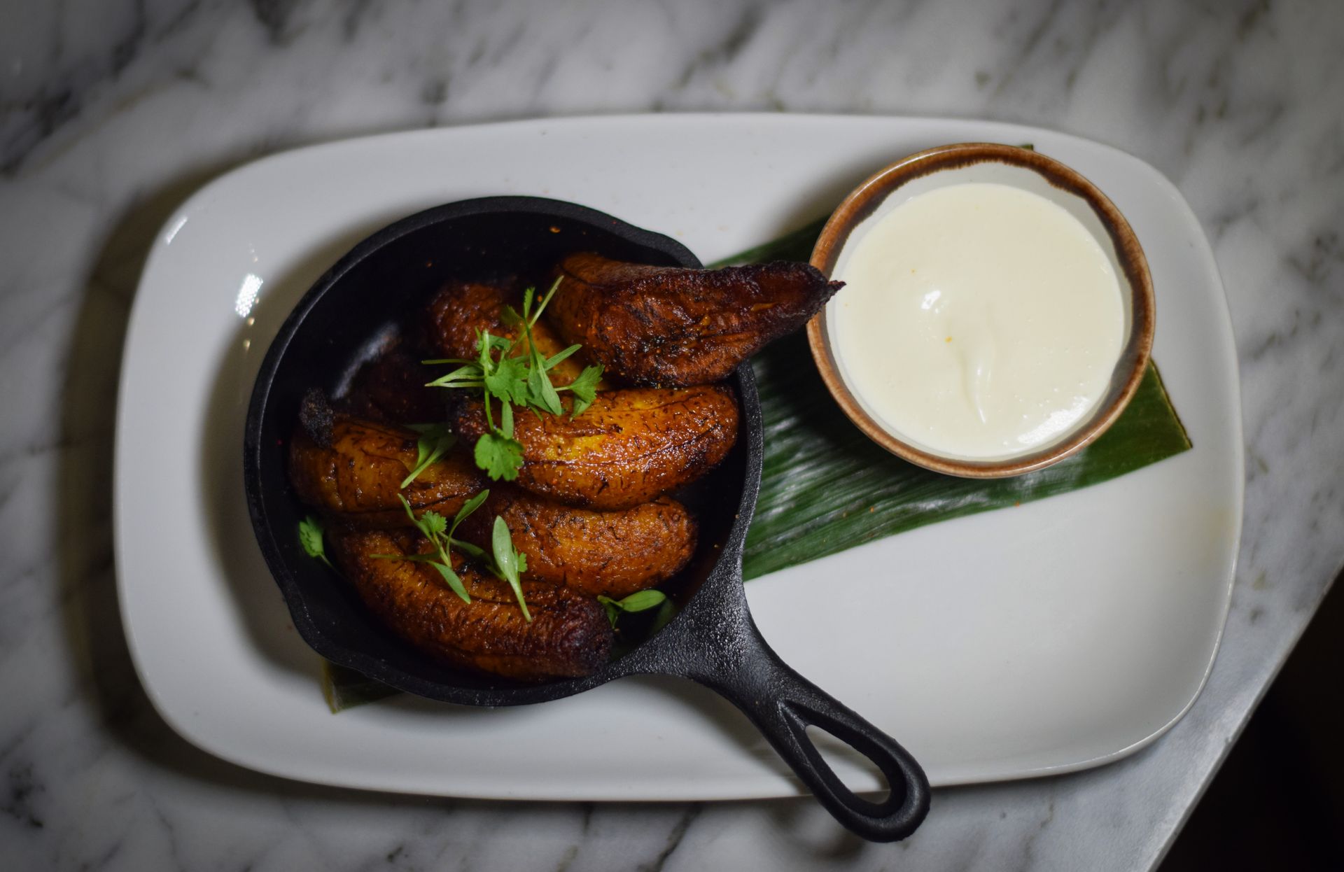 A white plate topped with fried bananas and a bowl of sour cream.