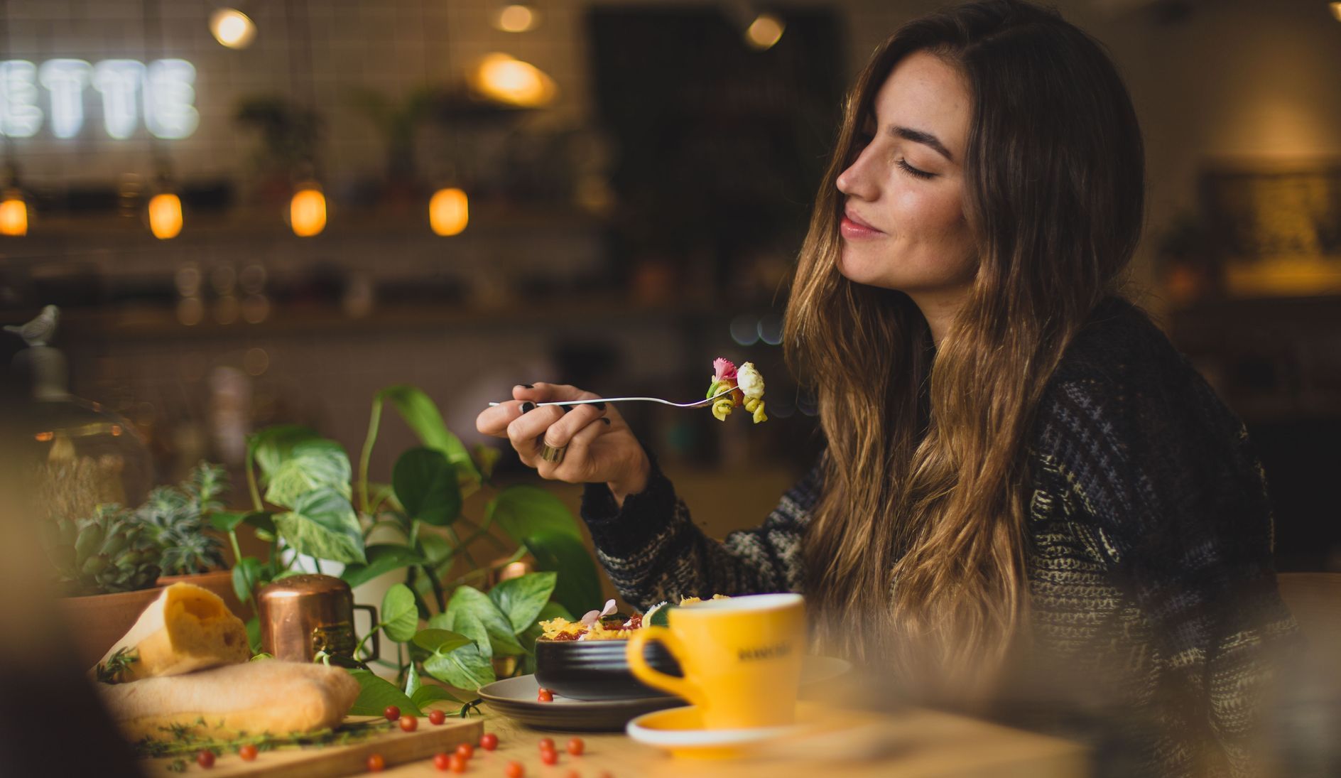 A woman is sitting at a table eating food with a fork.