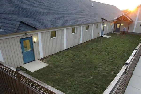 Backyard with green lawn, white-sided house, blue door, and wooden fence at sunset