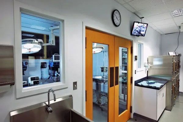 Hospital hallway with orange doors, sink, monitor, and medical equipment in a clean clinical room