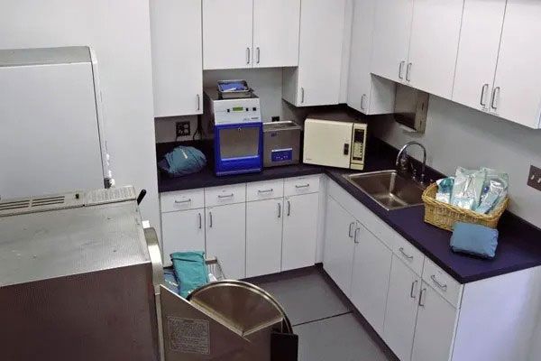 Small white kitchenette with cabinets, countertop appliances, sink, and a stainless-steel fridge.