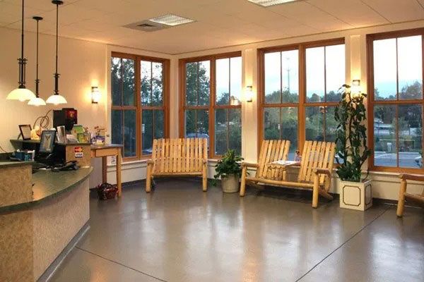 Bright lobby with large windows, wooden chairs, and polished concrete floor