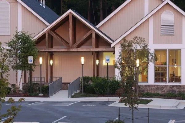 Apartment building entrance with peaked wooden awning, lit porch lights, and landscaped walkway at dusk