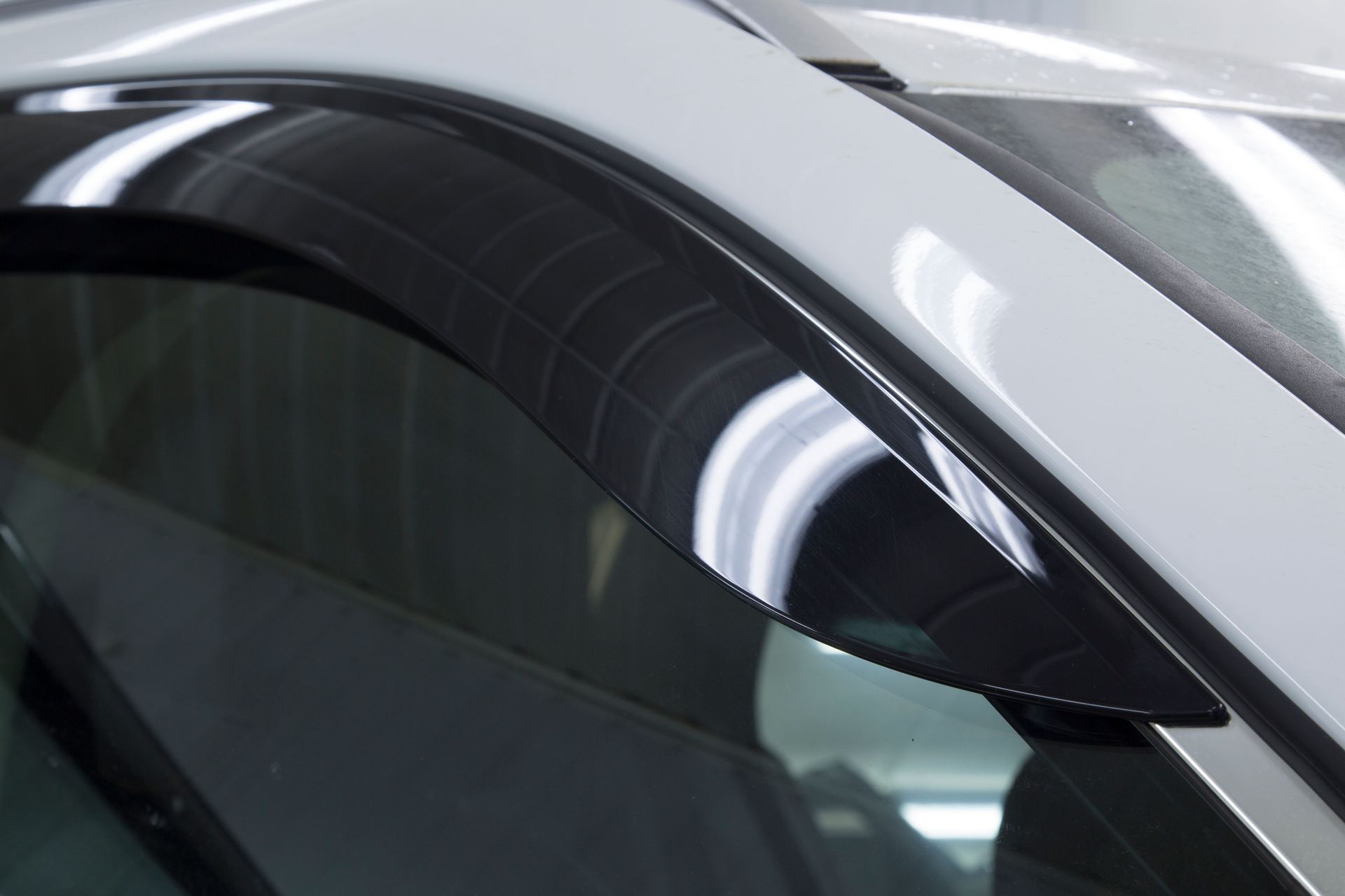 A white car with a black rain visor installed above the window.