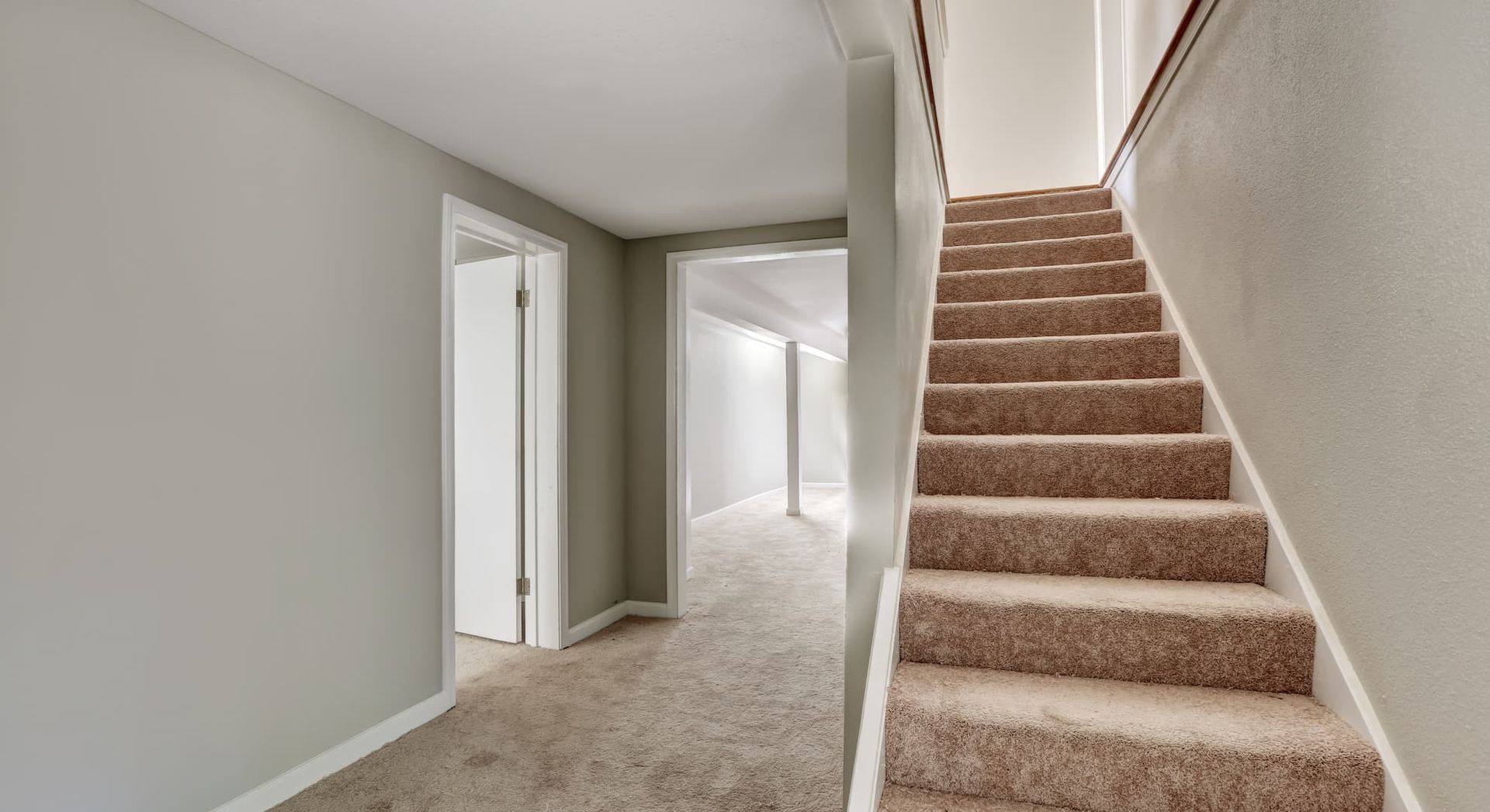 Hallway with stairs and doorway. Beige carpet on stairs and floor, grey walls.
