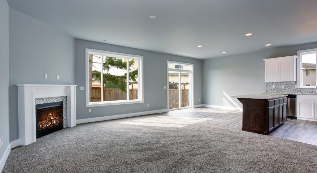 Spacious room with fireplace, windows, and kitchen island; light blue walls and gray carpet.