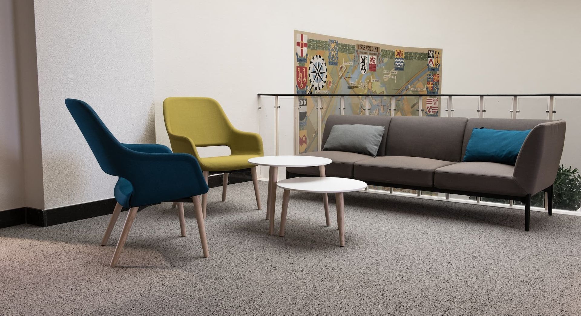 Living room with gray sofa, teal chair, yellow chair, white tables, and rug art.