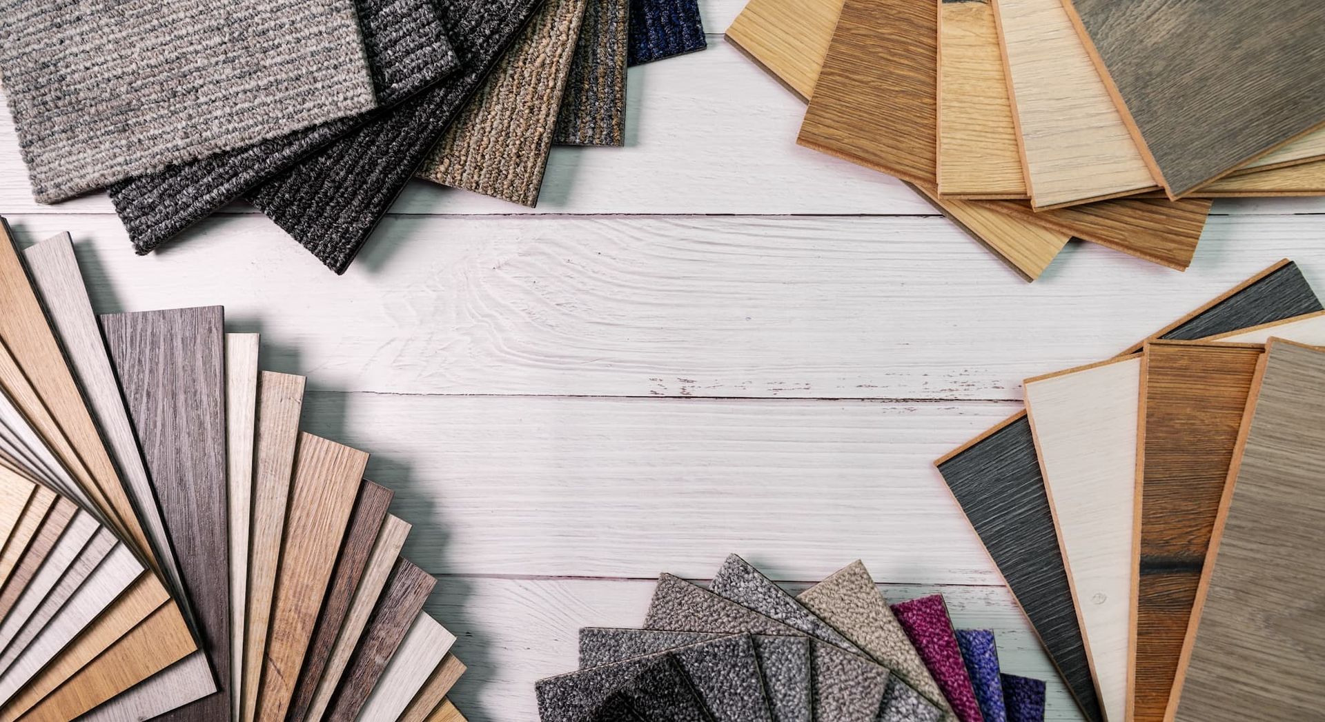 Assortment of flooring samples arranged on a white wooden surface. Various colors and textures, creating a display.
