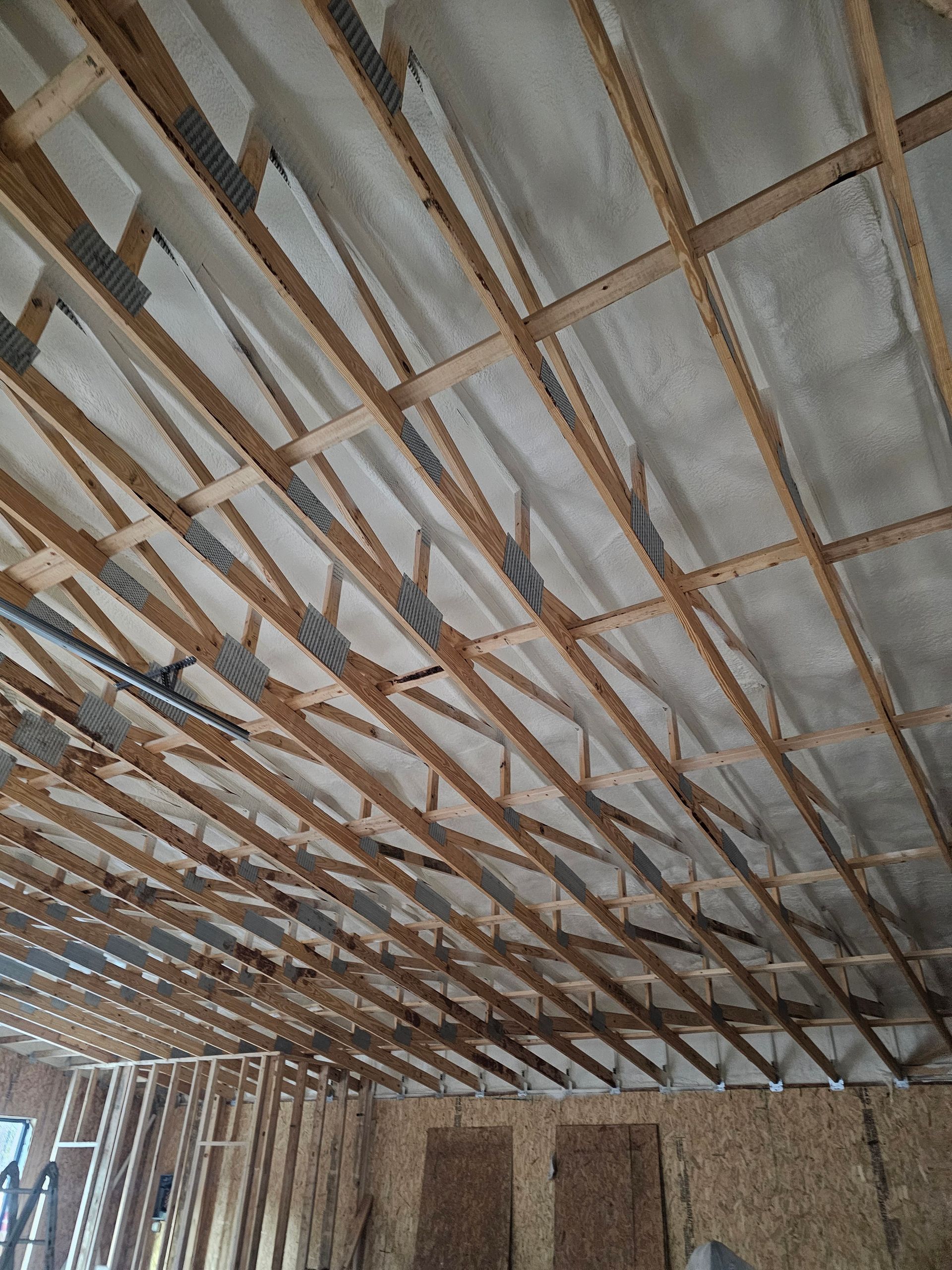 Exposed wooden roof trusses and sheathing seen from inside a room under construction with unfinished wall framing.