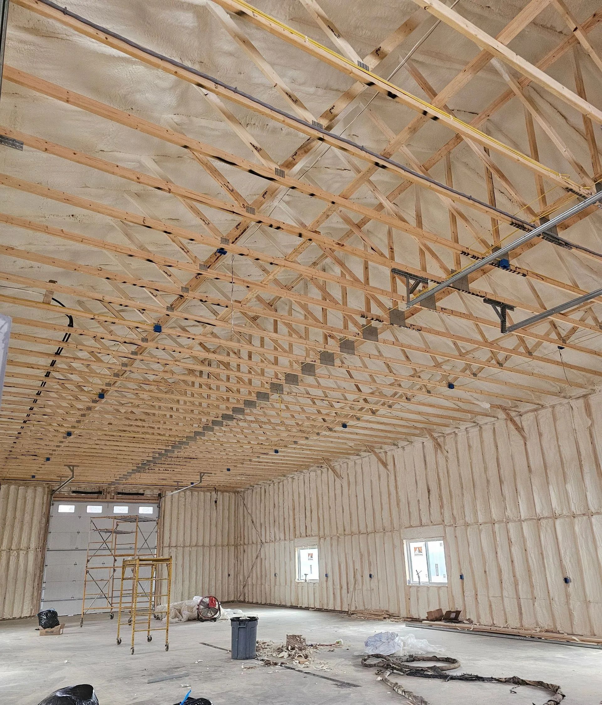 Interior of a large building under construction featuring exposed wood roof trusses and walls lined with foam insulation.