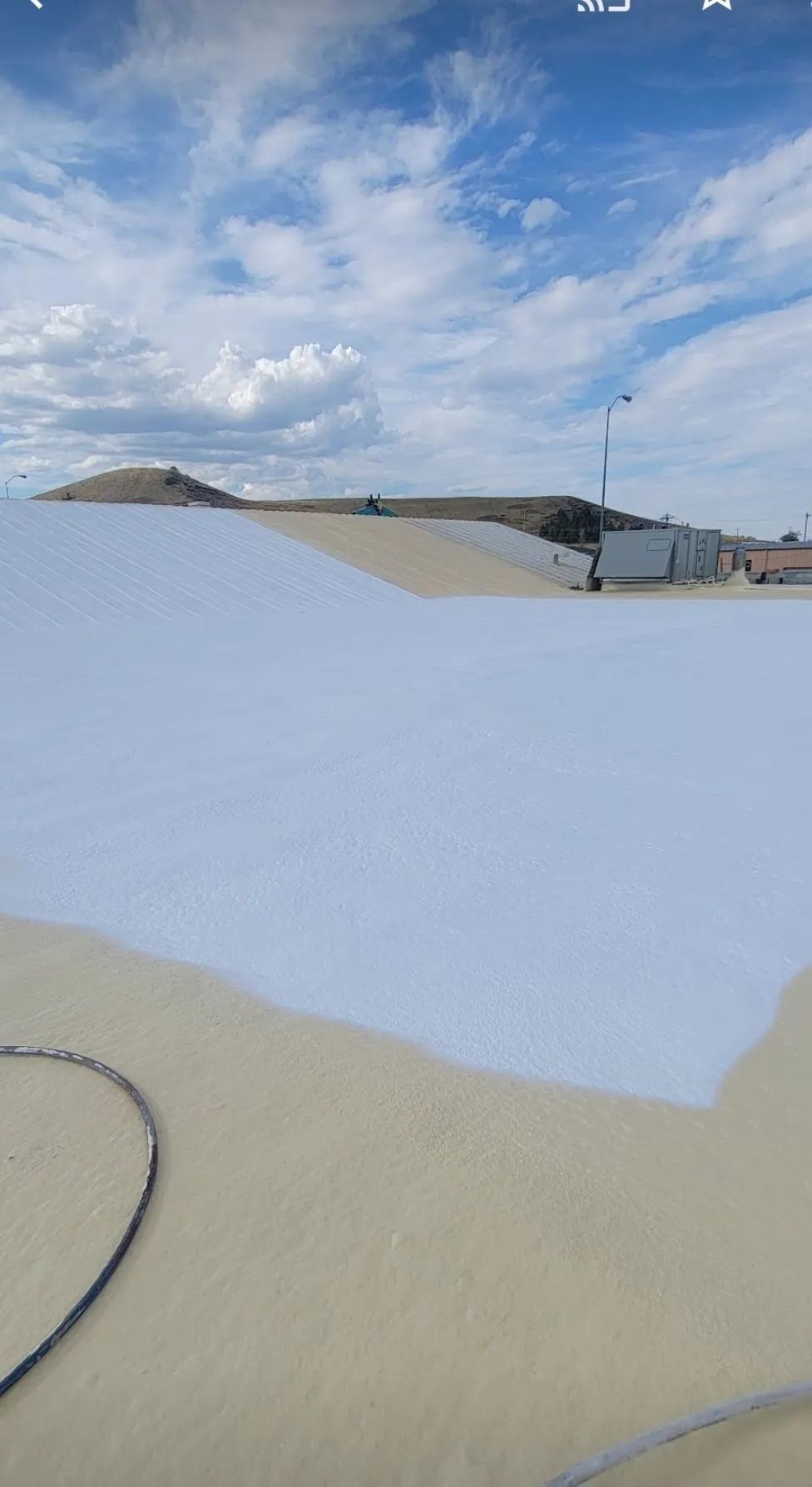 A large area of light-colored ground is partially covered by a smooth, white surface against a blue, cloudy sky.