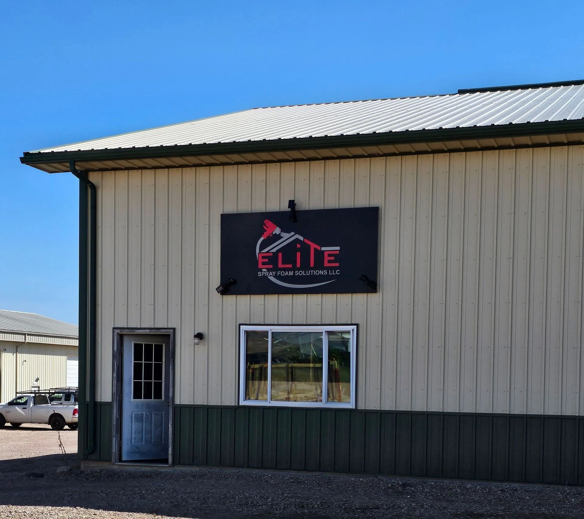 The exterior of a beige metal building with a dark green base, featuring a sign reading 