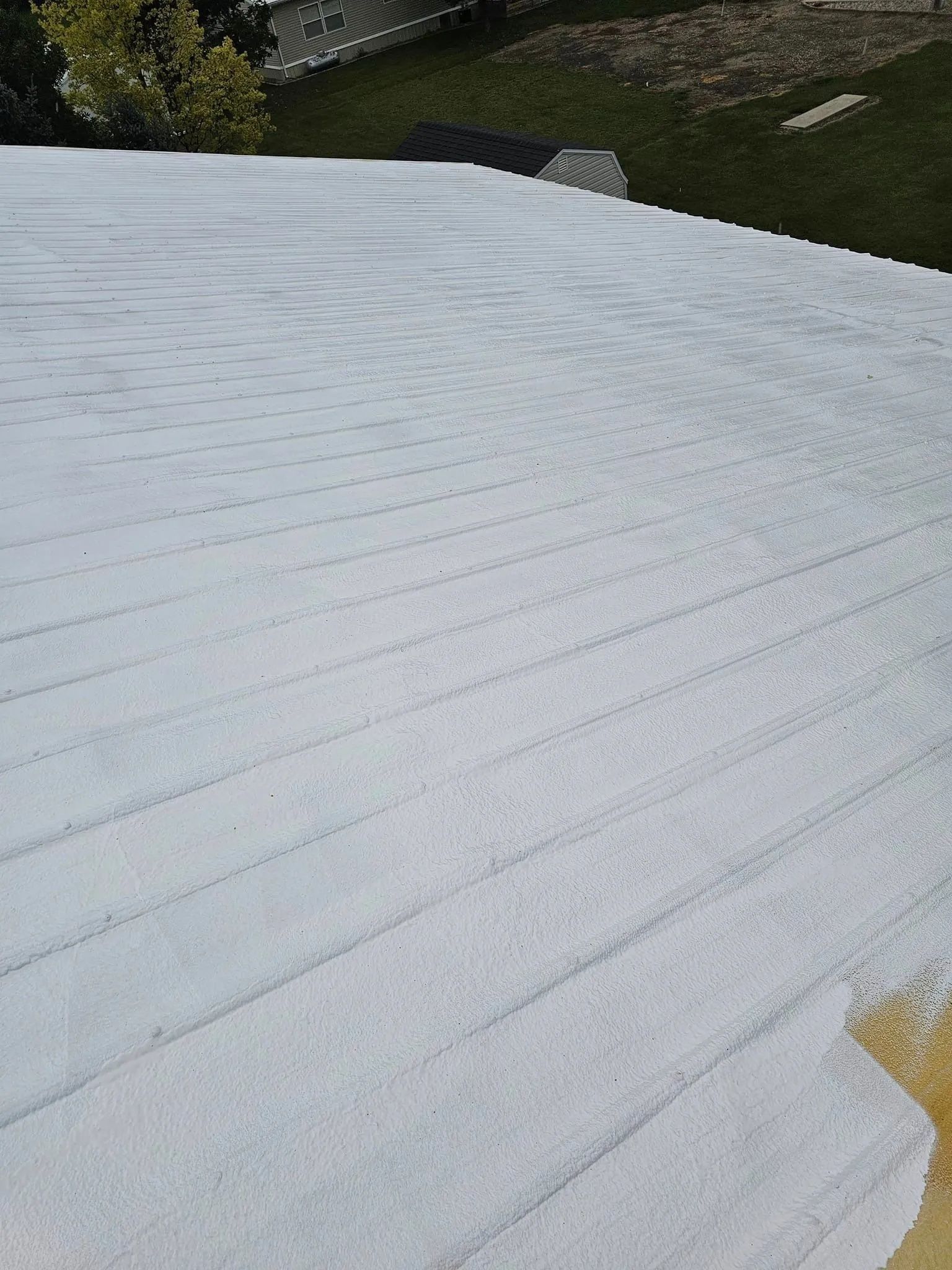 A sloped roof coated in white paint, showing distinct horizontal rows where the roller was applied.