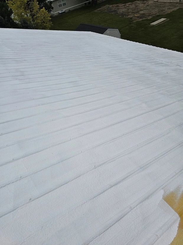 Snow-covered roof with a stone wall and grassy yard in the background