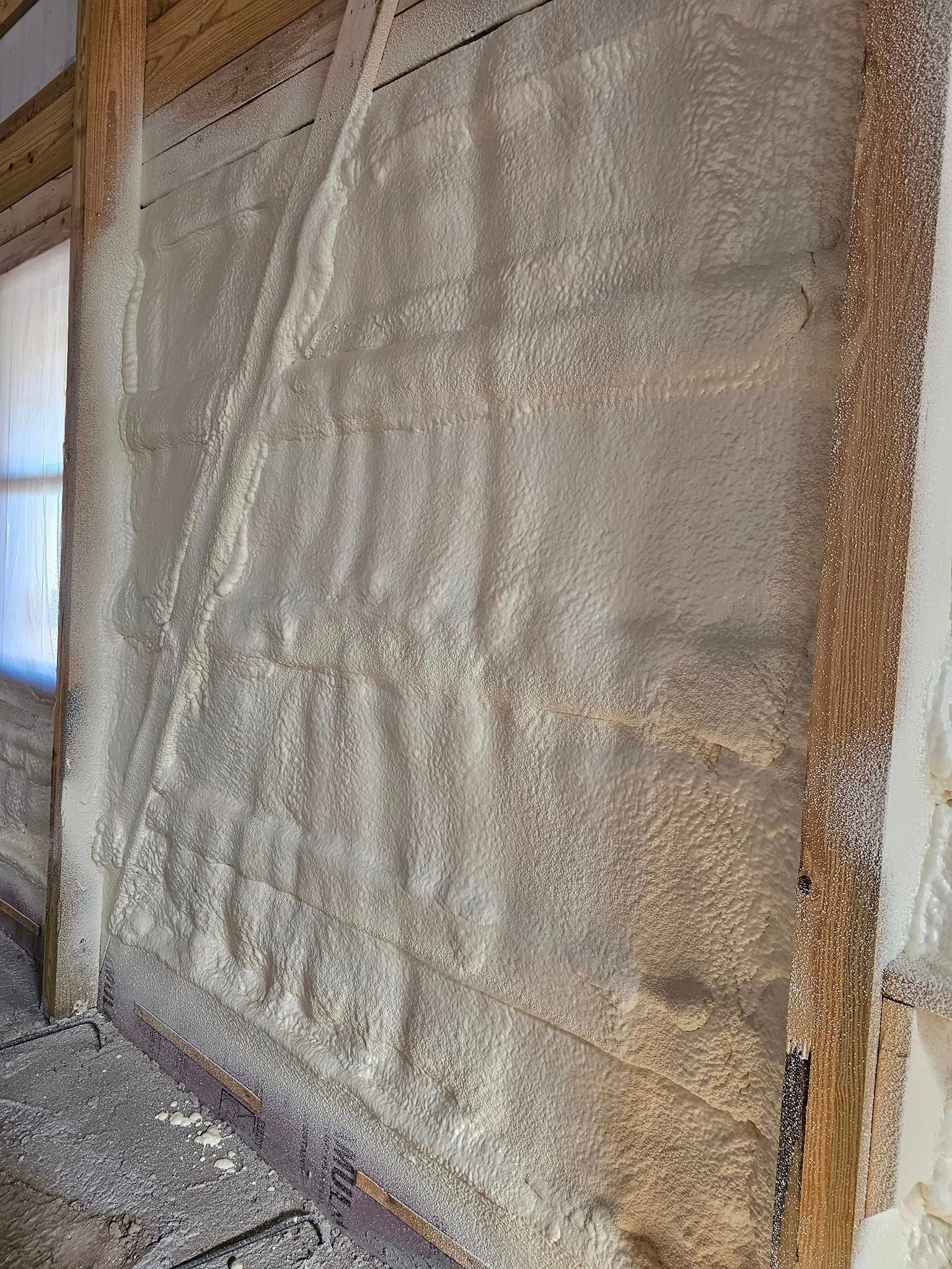 Textured, beige spray foam insulation applied between wooden wall studs inside a room.