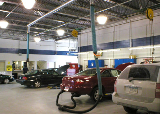Cars being worked on in a well-lit auto repair shop with ceiling-mounted hoses and tools.
