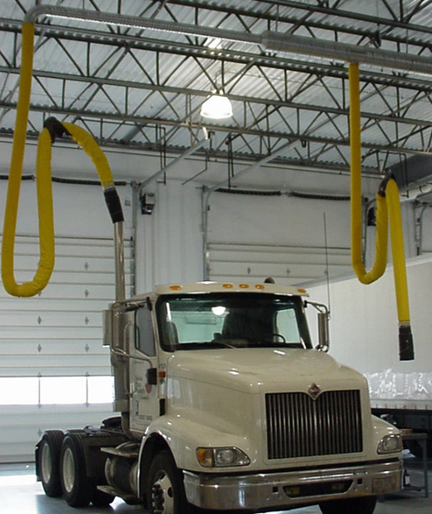 White semi-truck parked in a large garage, with yellow exhaust extraction arms suspended from the ceiling.