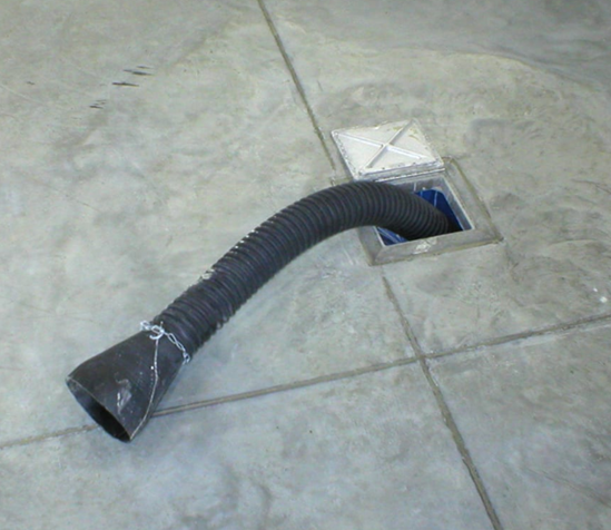 Black corrugated hose extending from a floor drain in a concrete floor. The drain cover is partially open.