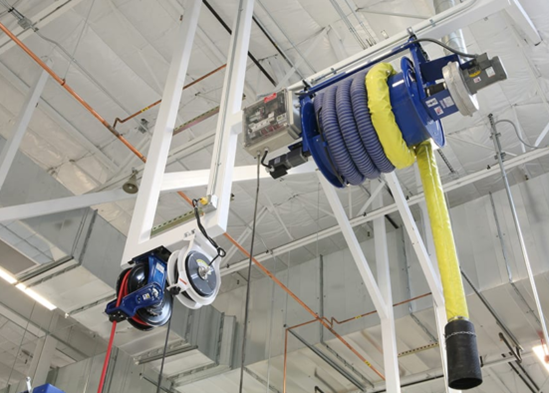 Ceiling-mounted industrial vacuum system with yellow and blue hoses and a black nozzle.