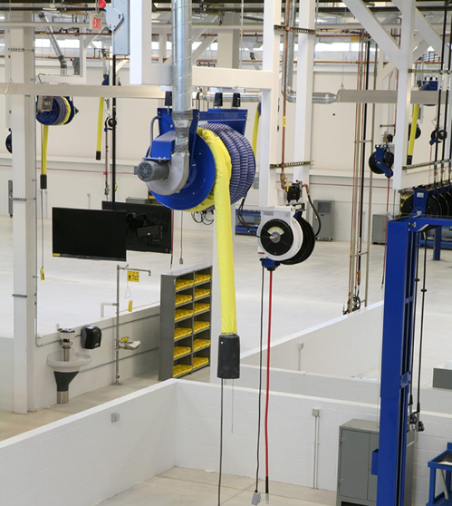 Overhead industrial cable management system in a factory setting, featuring yellow coiled cables and blue/gray machinery.